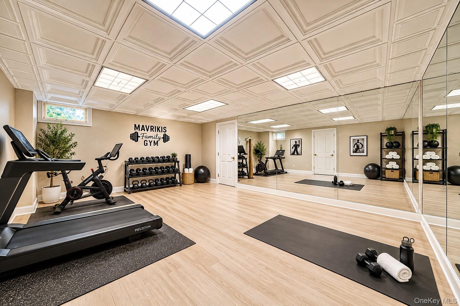 State-of-the-art home fitness studio featuring light wood-finish flooring, a full wall of mirrored panels, recessed and panel ceiling lighting, and a 
