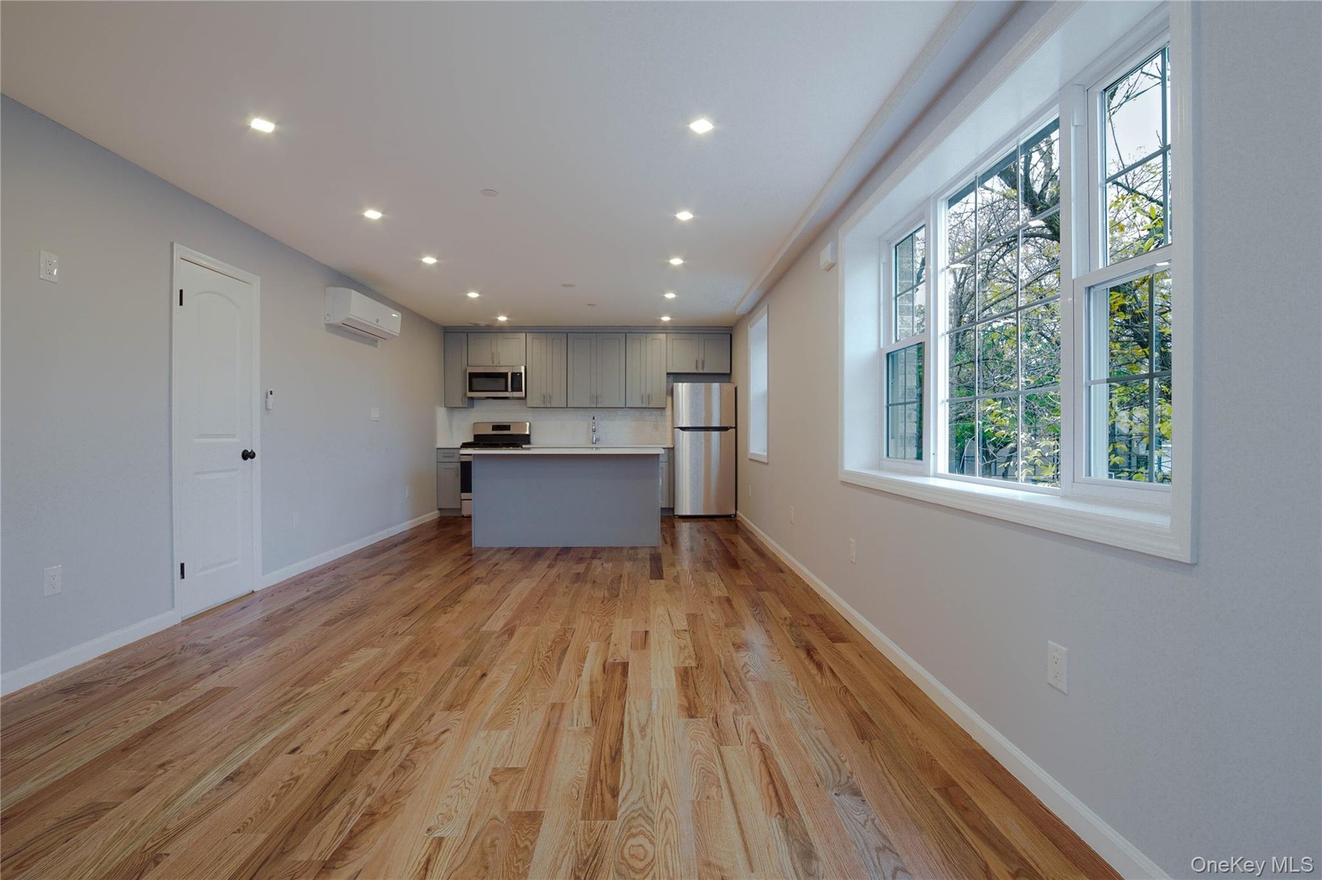 Kitchen featuring gray cabinetry, open floor plan, light countertops, light wood finished floors, and stainless steel appliances