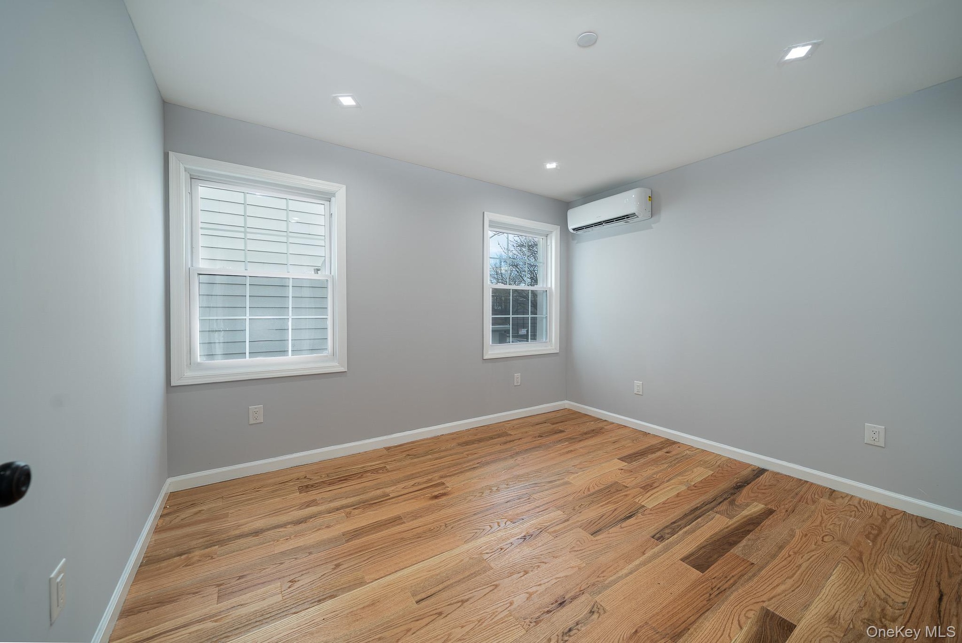 Empty room with light wood-type flooring and an AC wall unit