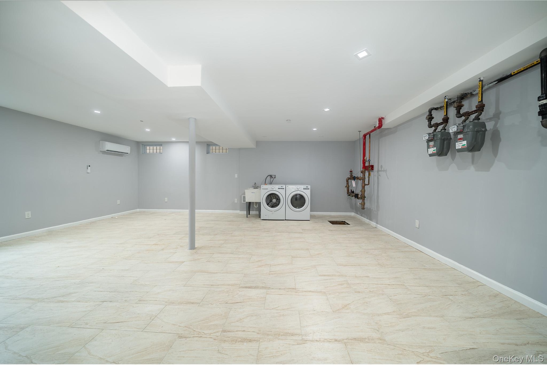 Finished below grade area with a wall mounted air conditioner, recessed lighting, and independent washer and dryer