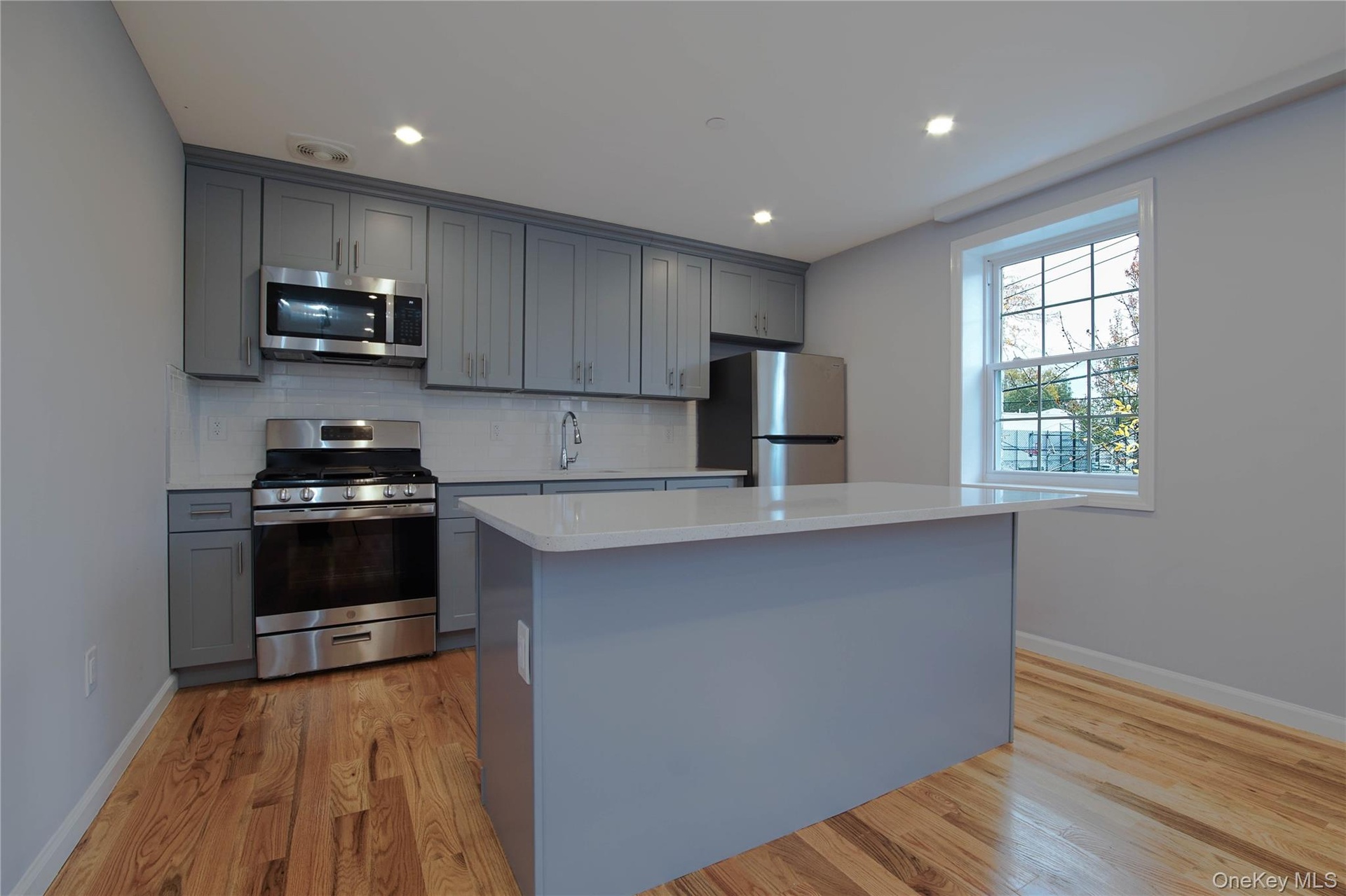 Kitchen featuring gray cabinetry, stainless steel appliances, tasteful backsplash, a kitchen island, and light wood-type flooring