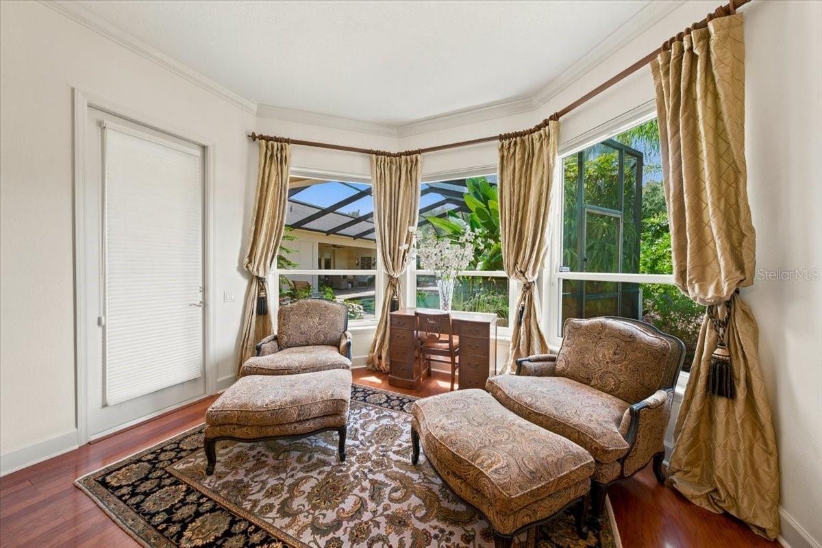Private primary sitting area featuring rich hardwood floors, expansive windows framing outdoor views, and elegant drapery.