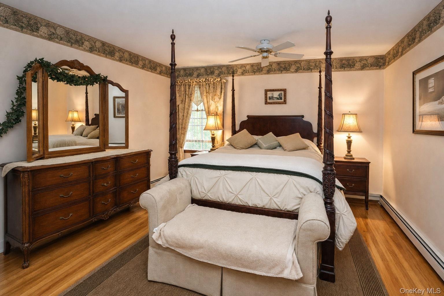 Wood-finish flooring, ceiling fan with integrated lighting, window with decorative drapery, and a classic dresser with an attached mirror