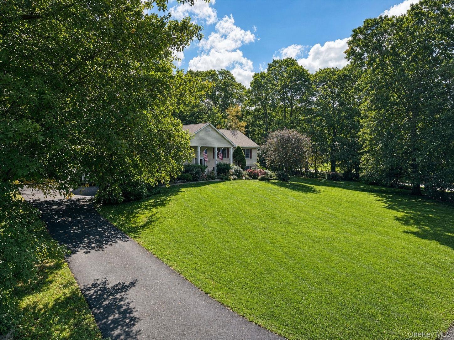 Expansive front lawn with mature trees and a paved driveway leading to the residence