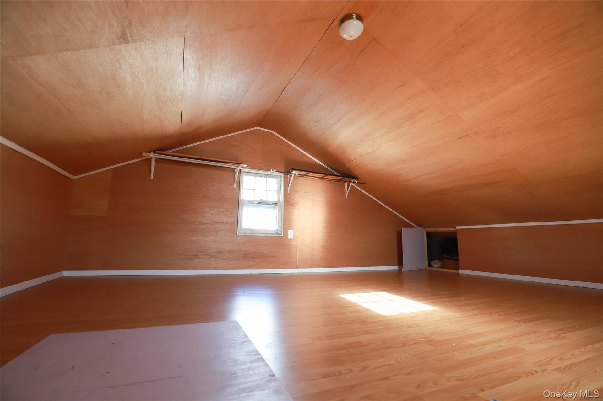Spacious attic room with vaulted ceiling, wood-finish flooring, and abundant natural light from dormer window