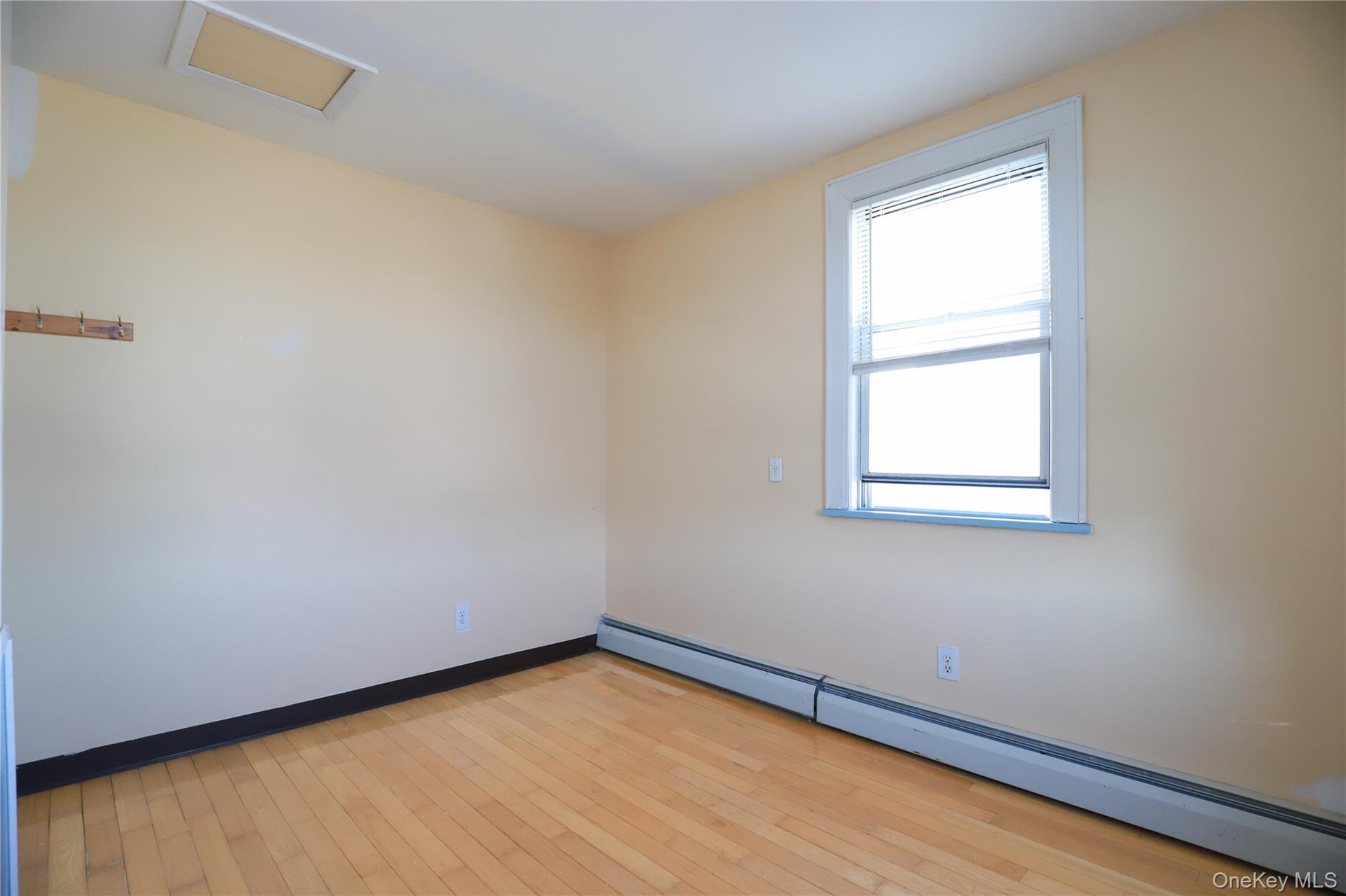 Bright corner room with wood-finish flooring, large double-hung window with natural light exposure, and clean walls with neutral finish