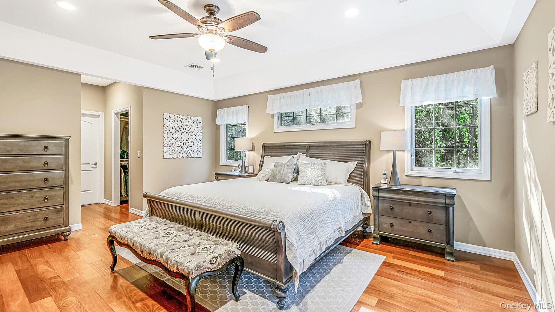 Tray ceiling with a ceiling fan, recessed lighting, and wood-finish flooring