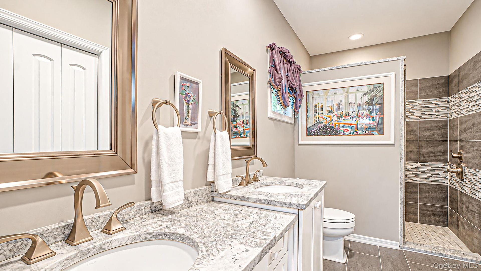Spa-inspired master bathroom featuring dual vanities with polished stone countertops, brass fixtures, and an undermount sink design - radiant heated f