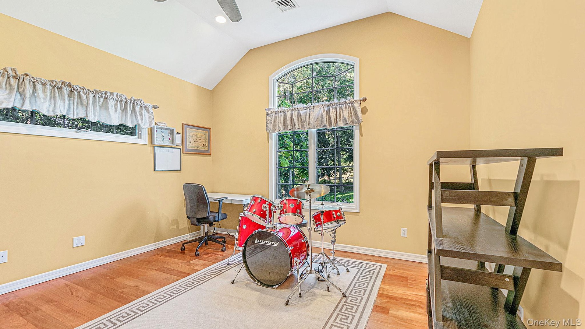 Vaulted ceiling with a ceiling fan, hardwood flooring, and an arched window