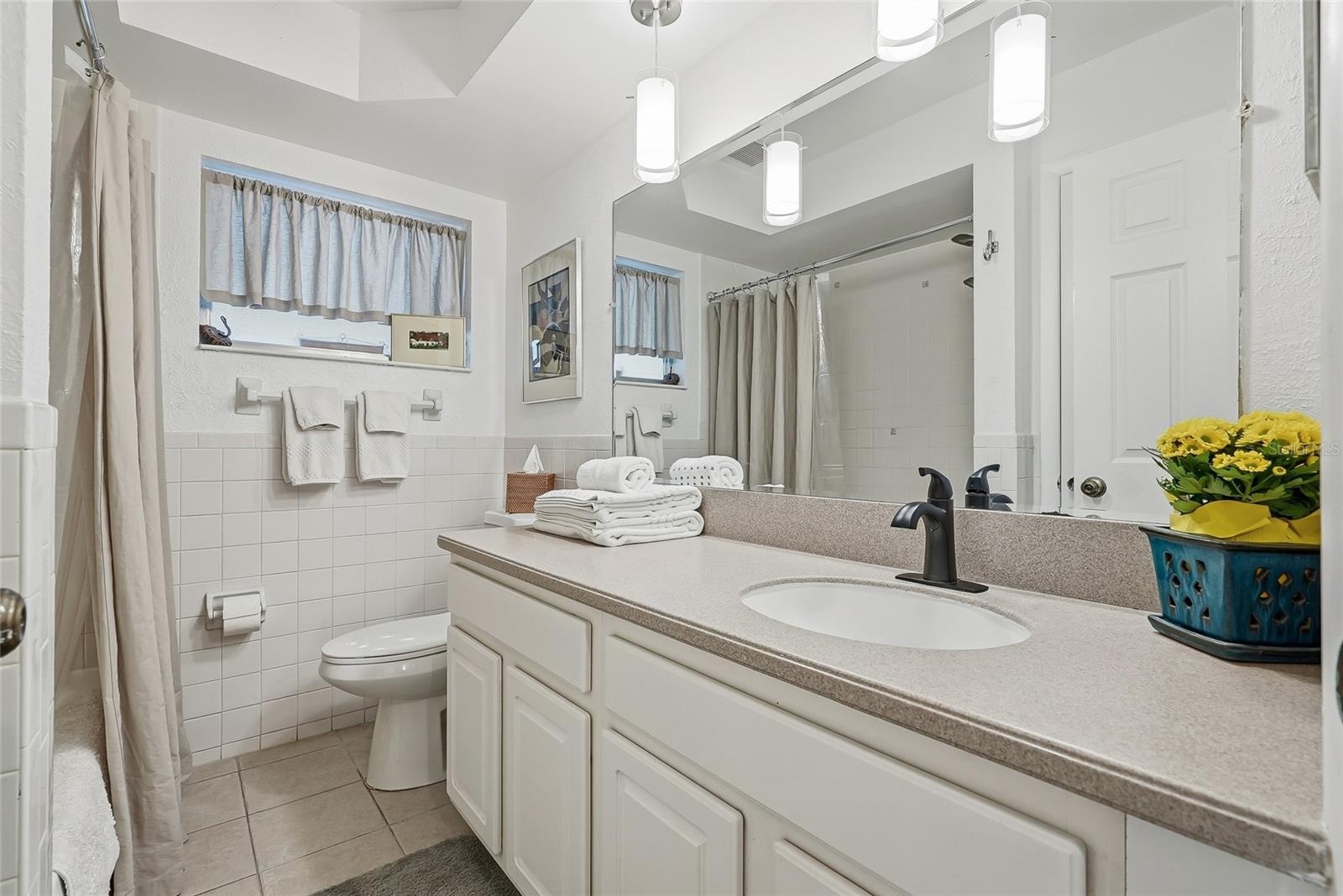 A generous vanity, broad mirror, and pendant lighting create a bright, comfortable space to get ready, with cabinet storage below.