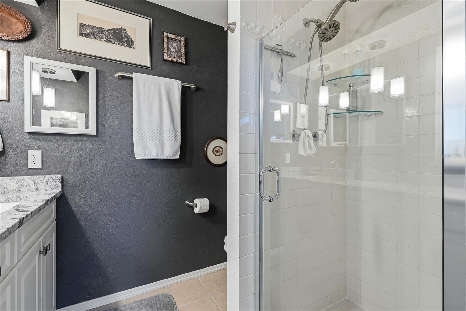 The primary bath features a glass-enclosed shower with classic white tile, glass corner shelves, and a convenient handheld showerhead.