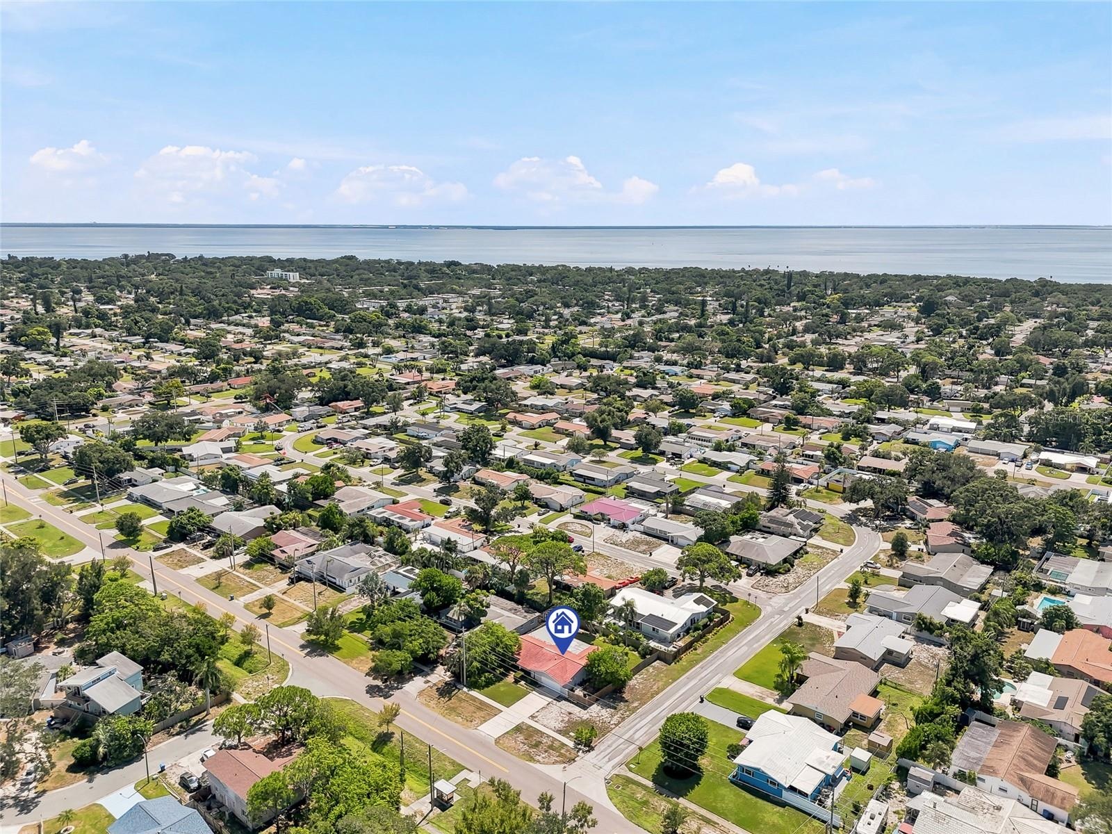 An elevated view highlights the home’s corner lot and tree-filled surroundings, with the bay forming a scenic backdrop beyond the neighborhood.