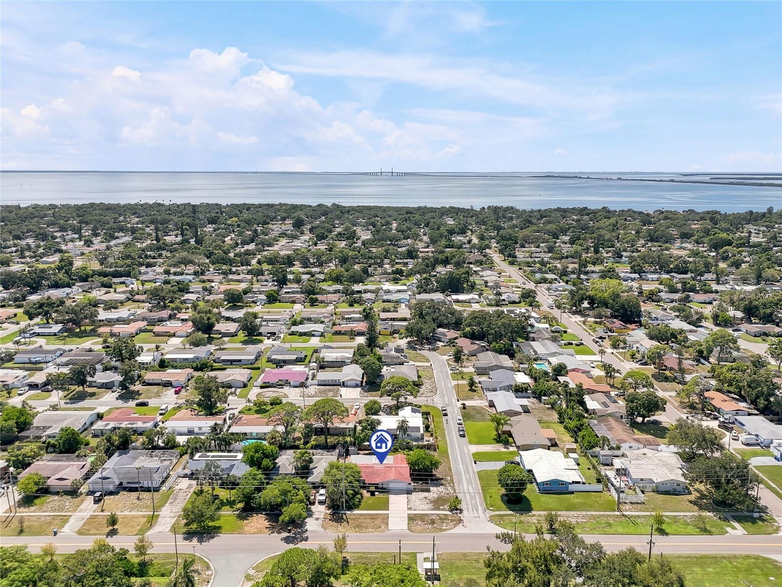 A wider aerial perspective places the home within its leafy St. Petersburg neighborhood, with the bay and Sunshine Skyway Bridge on the horizon.