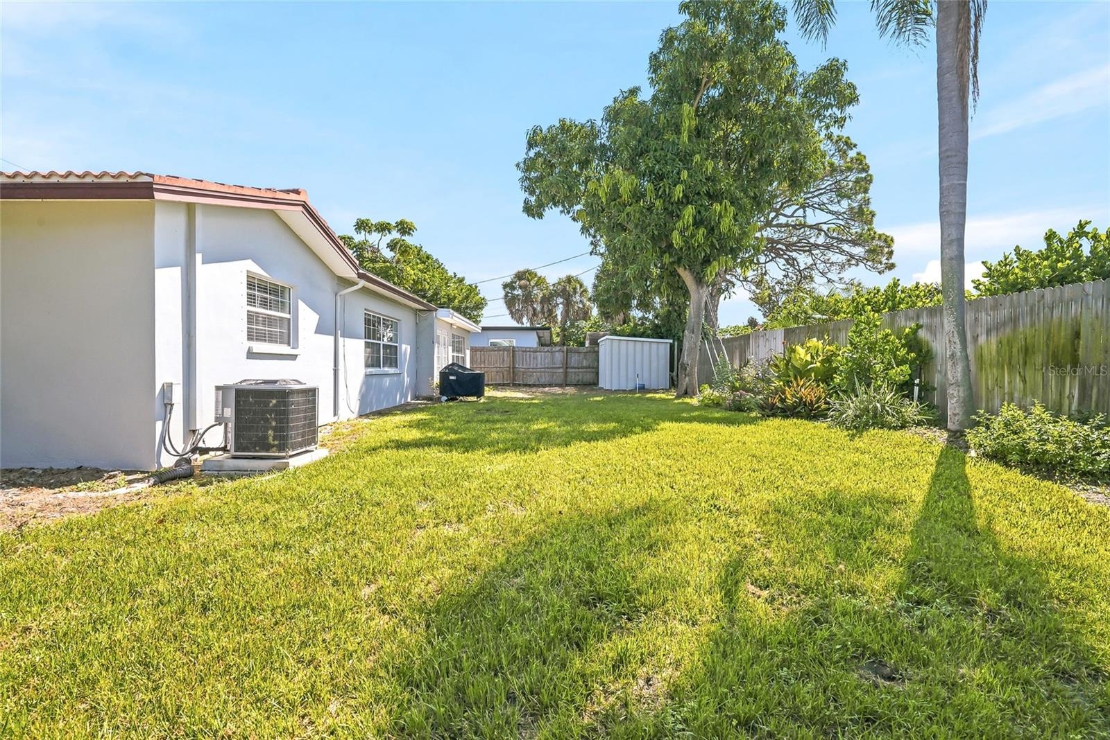 Stretch out in the sunshine or settle beneath the trees, with open lawn, established planting beds, and wood fencing framing the backyard.