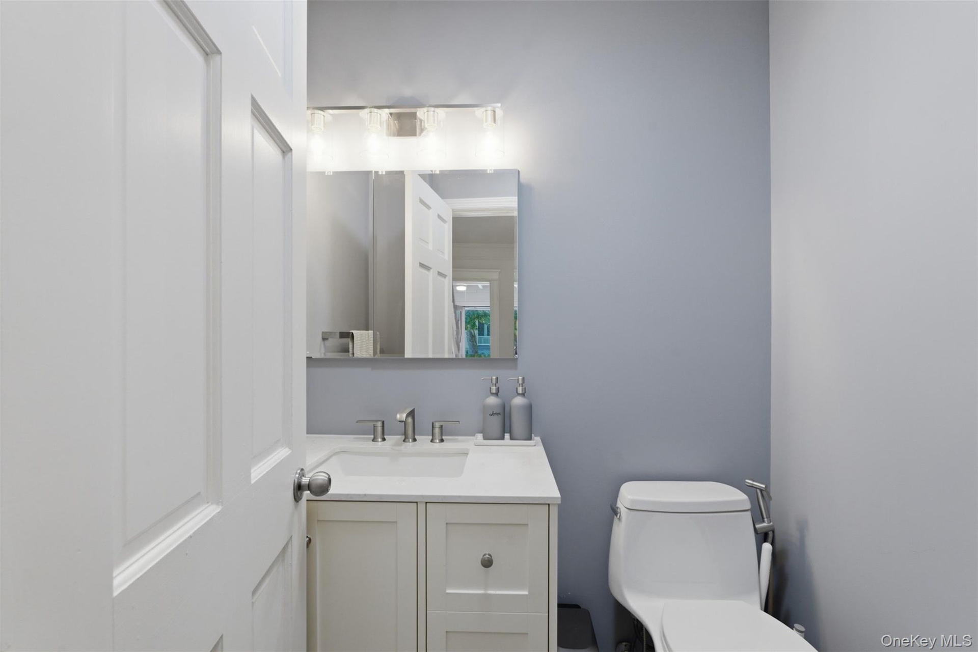 White vanity with an integrated sink and brushed nickel faucet, illuminated by a vanity light fixture over a rectangular mirror