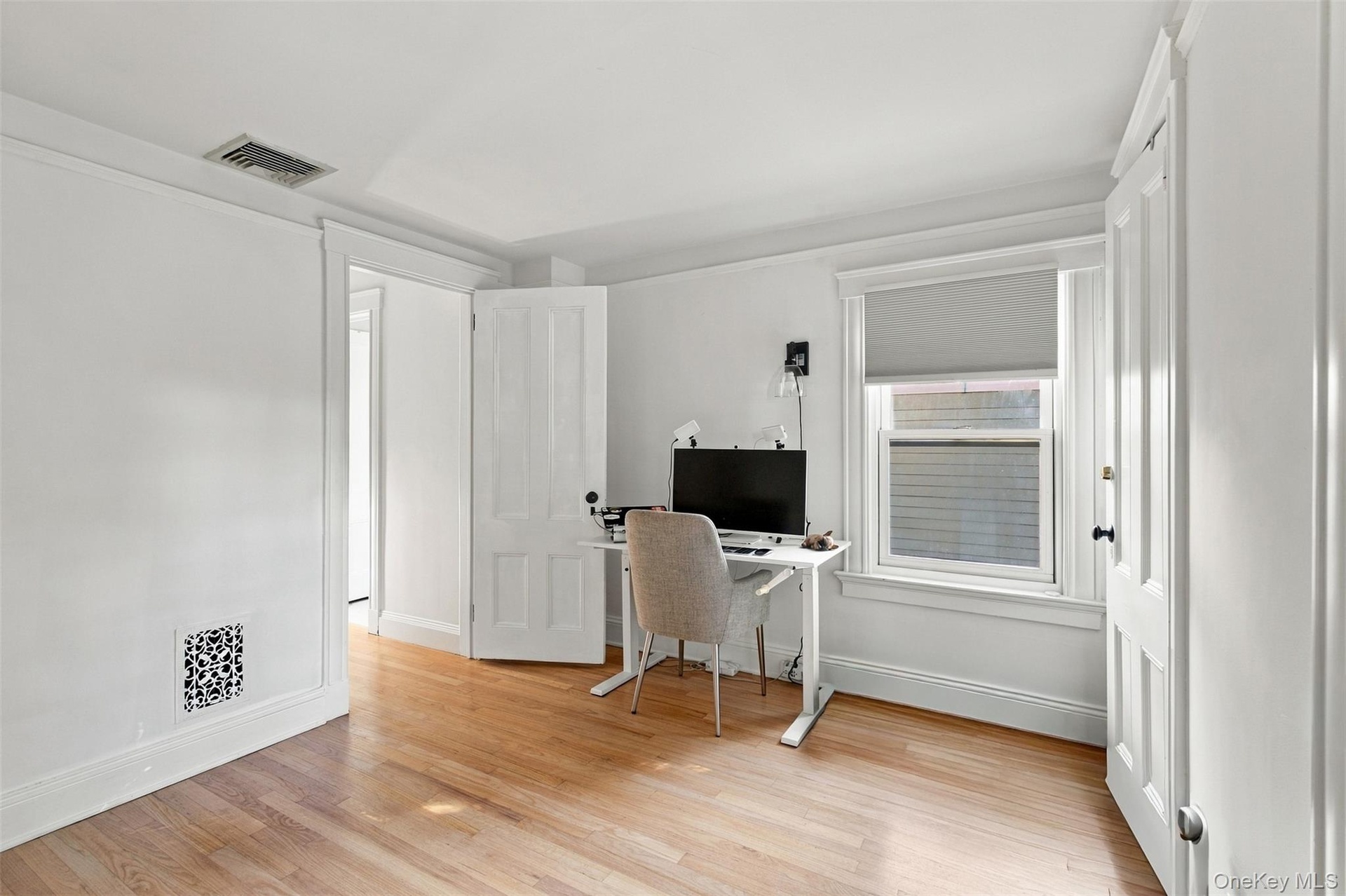 Hardwood flooring, painted paneled door, single window with white trim, white walls, and crown molding