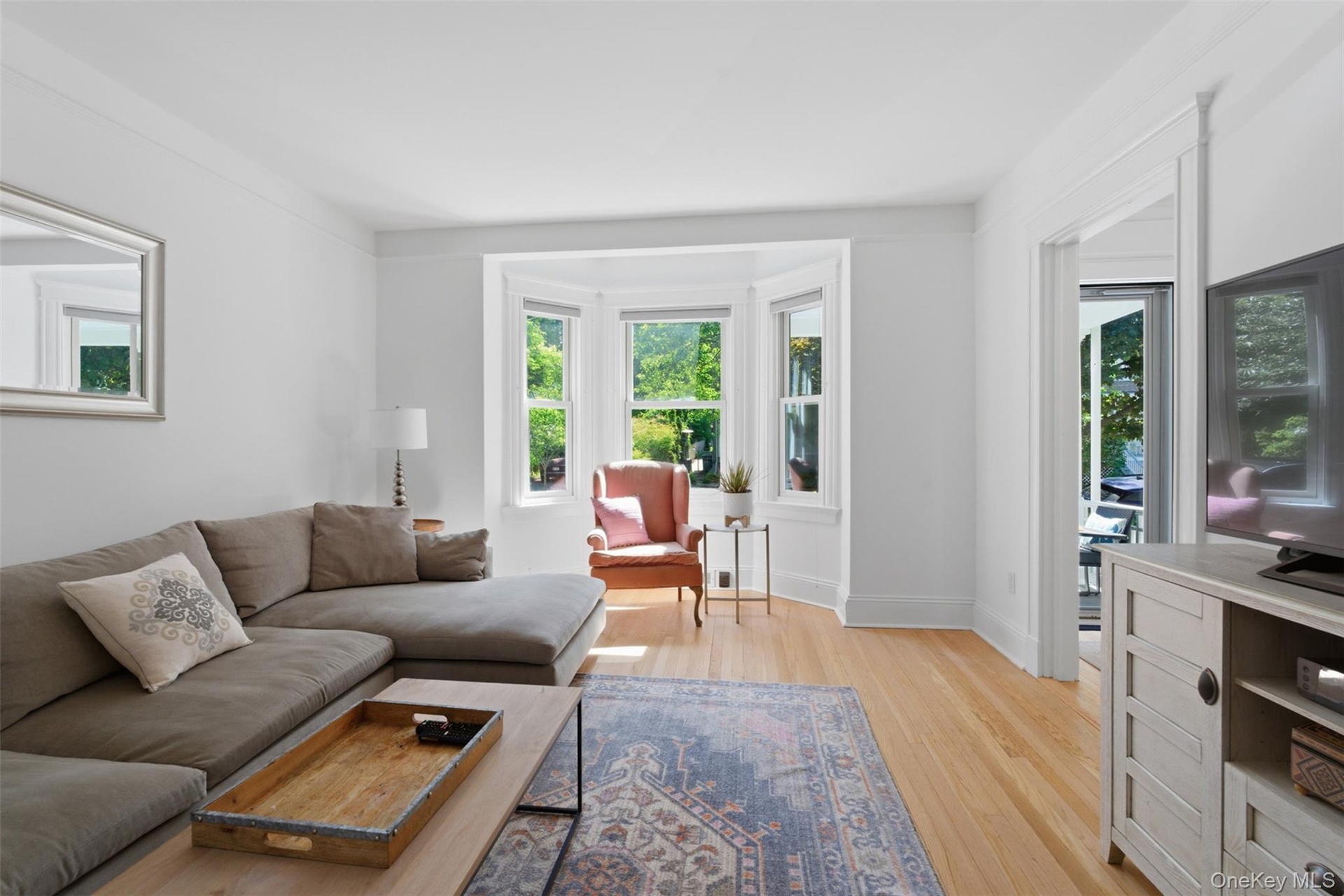 Hardwood flooring, bay window, crown molding, white trim, and a doorway with French doors
