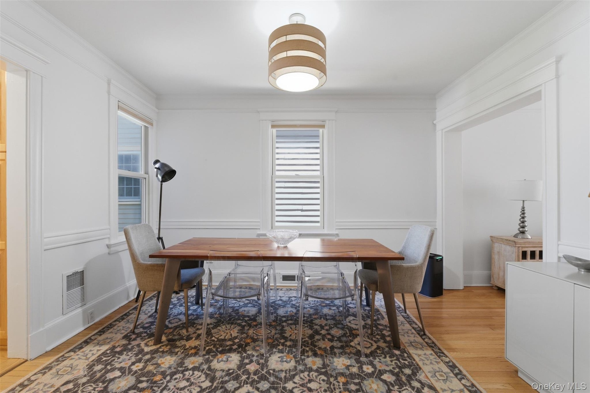 Hardwood flooring paired with white walls, decorative crown molding, and a drum pendant light fixture