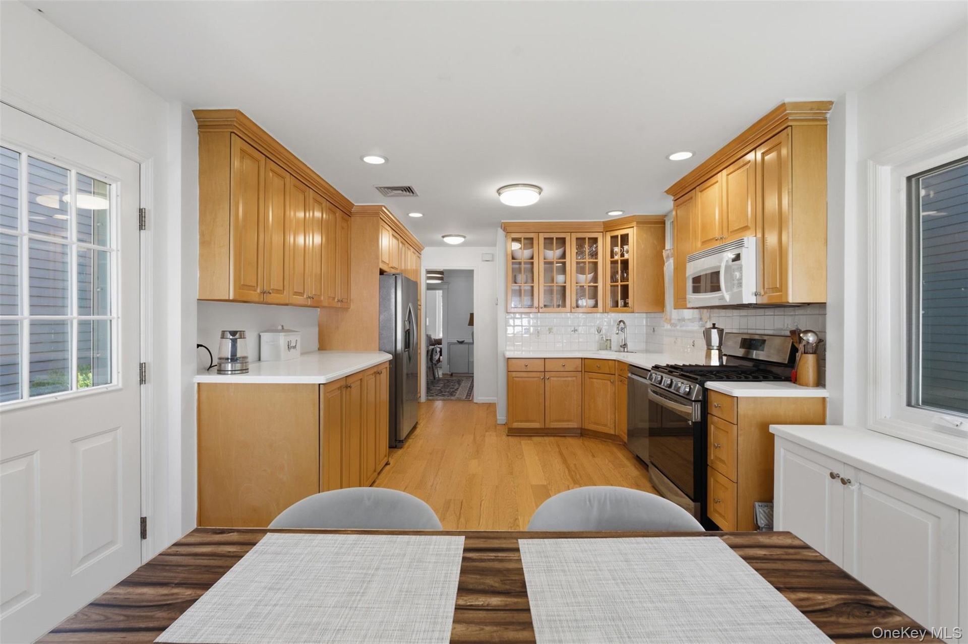 Light wood cabinetry, stainless steel appliances, white subway tile backsplash, recessed lighting, and wood-finish flooring