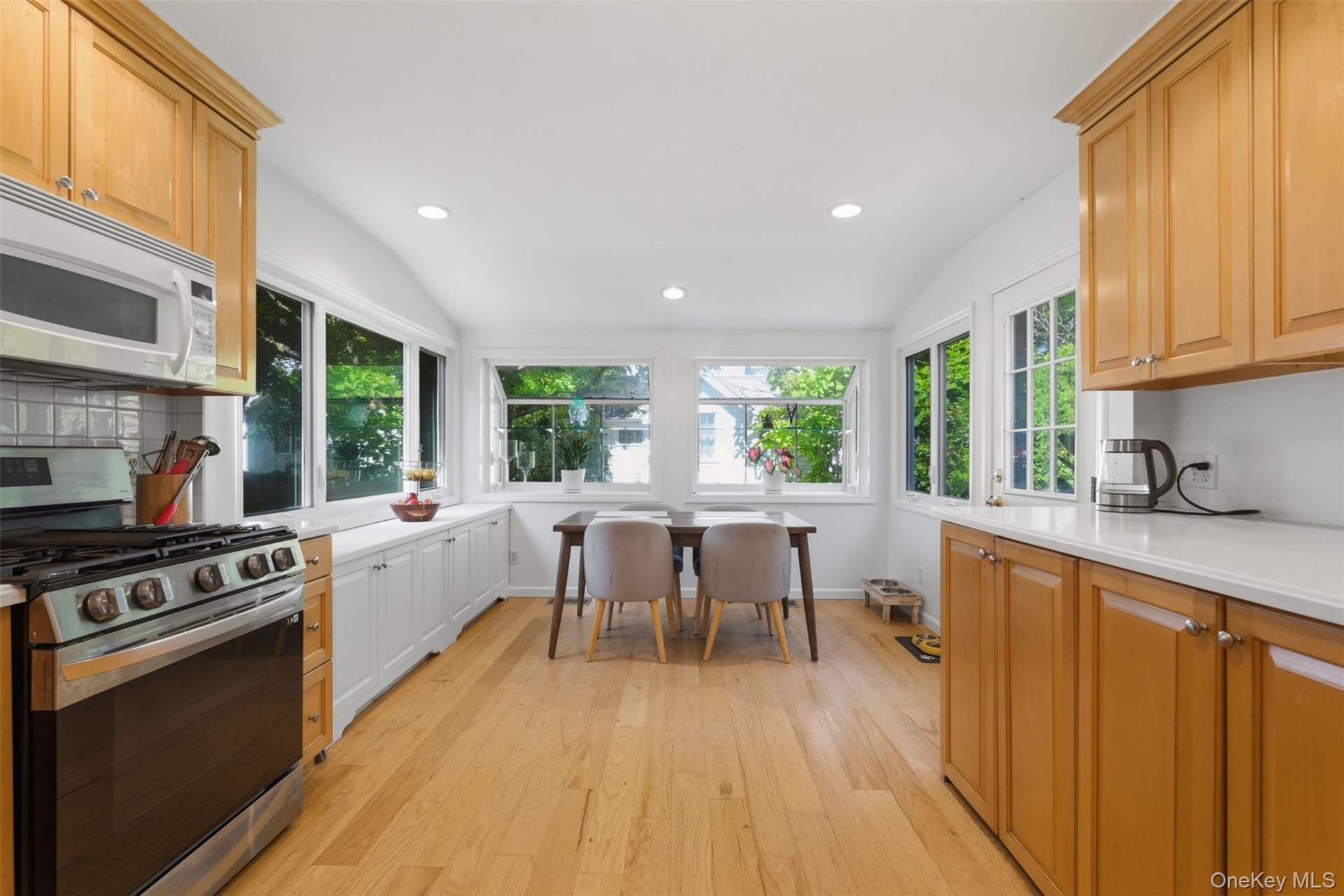 Vaulted ceiling, recessed lighting, wood-finish flooring, white countertops, and stainless steel appliances