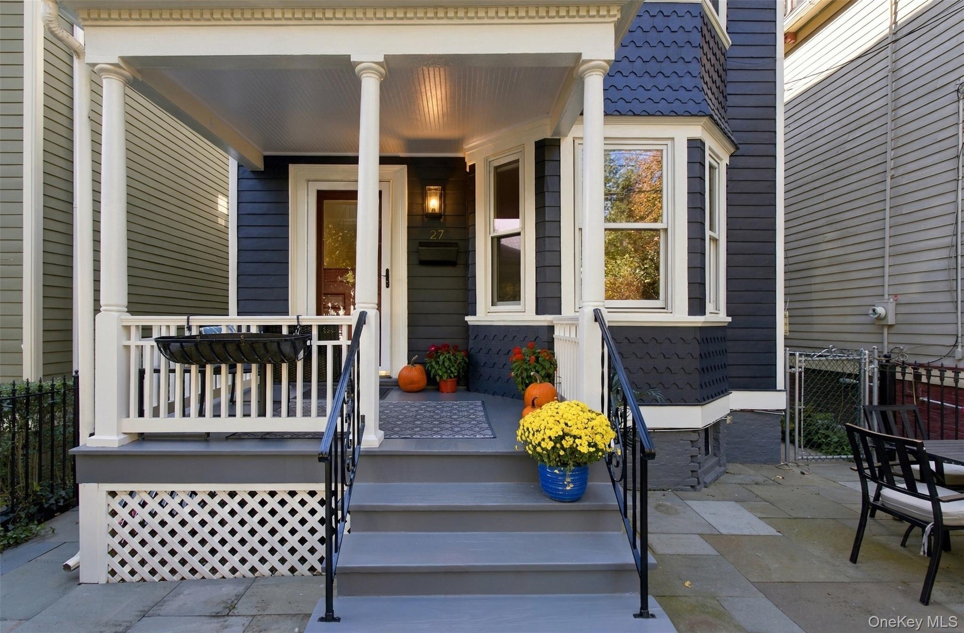 Covered front porch with white columns, wood siding exterior, bay window, stone tile patio, and wrought iron railing