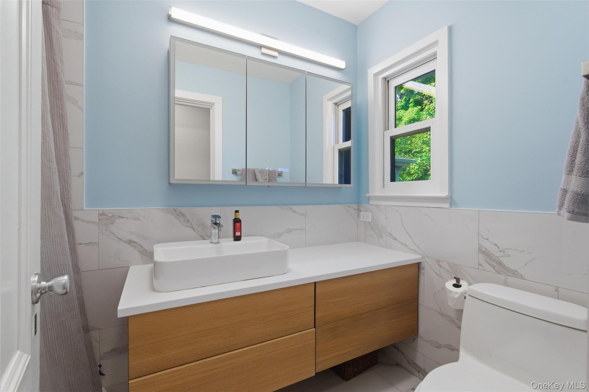 Floating wood-finish vanity with a vessel sink, white countertop, and wall-mounted medicine cabinet
