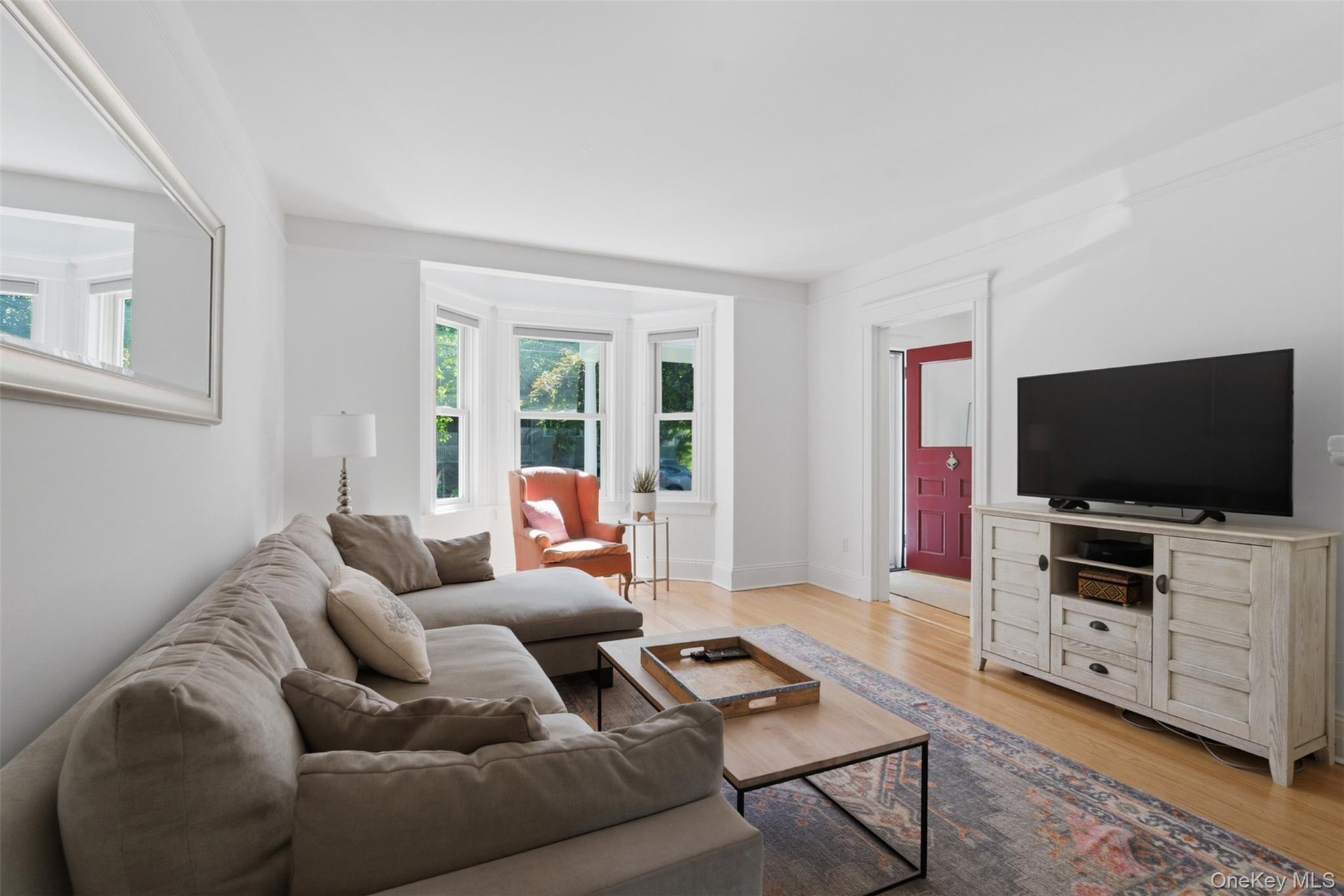 Hardwood flooring, bay window, white trim, recessed lighting, and a painted paneled door