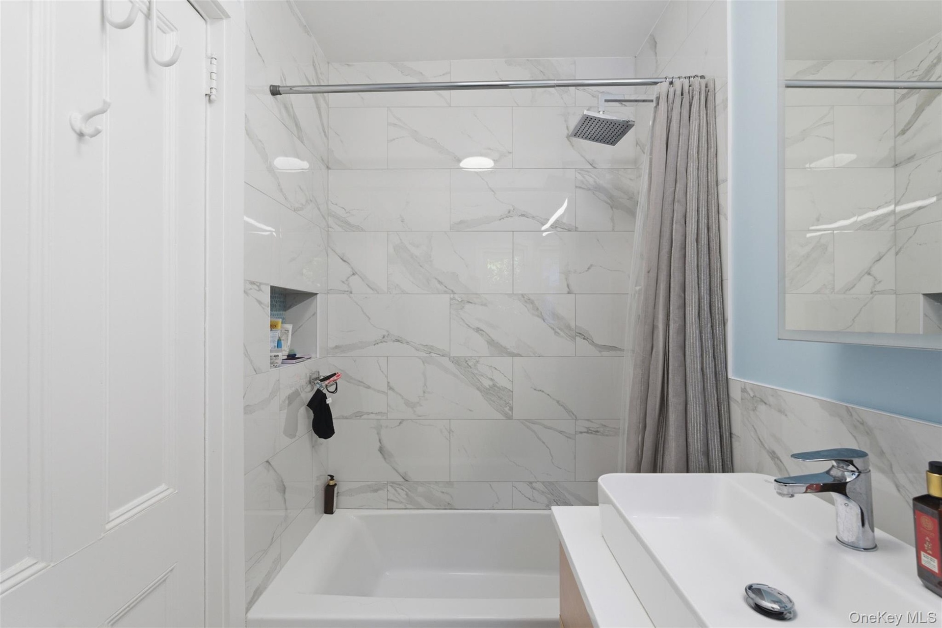 Bathroom featuring a white rectangular bathtub, white tiled shower surround with a built-in niche, modern square rain shower head, and a white rectang