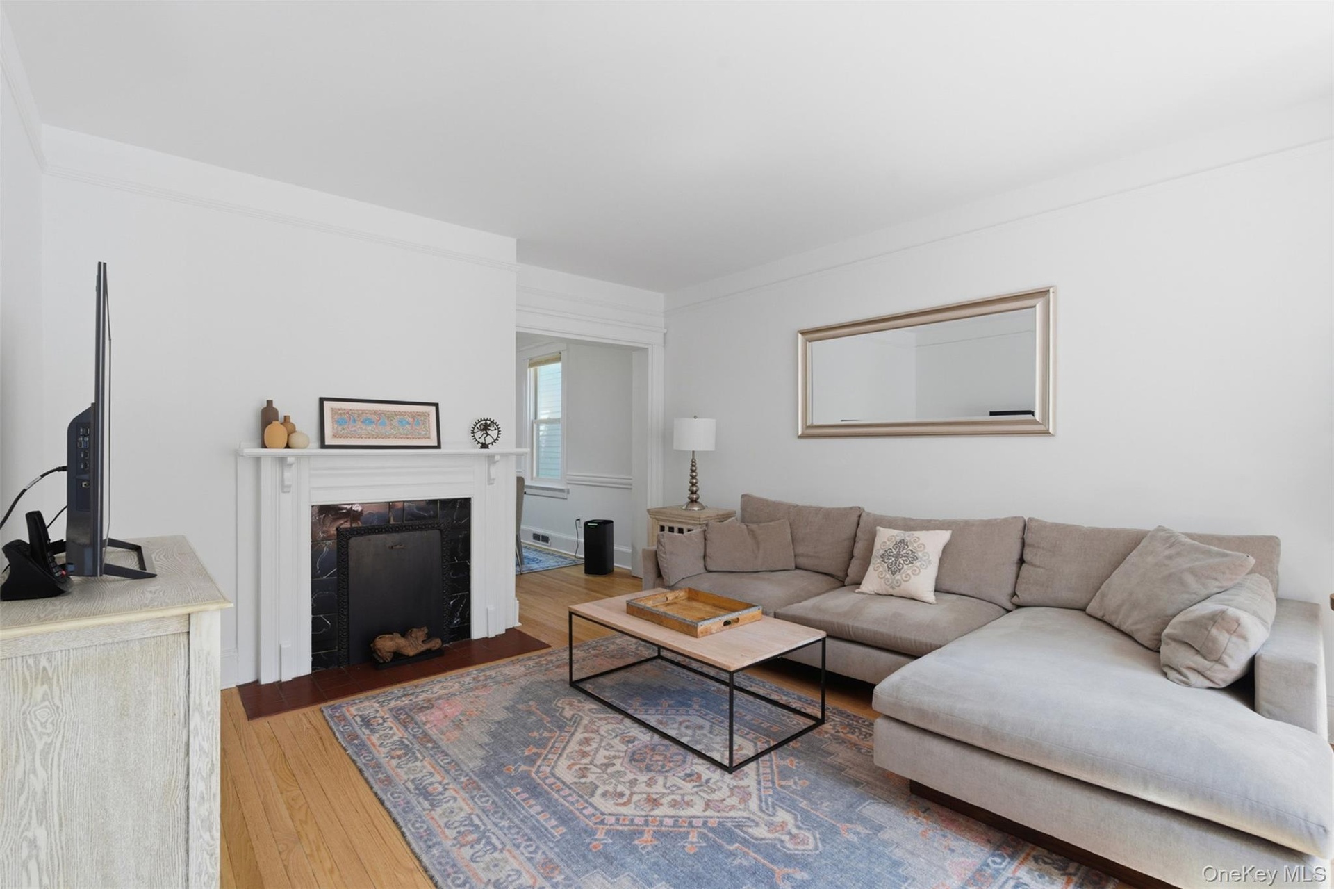 Hardwood flooring, crown molding, and a fireplace with a white mantel and dark stone surround