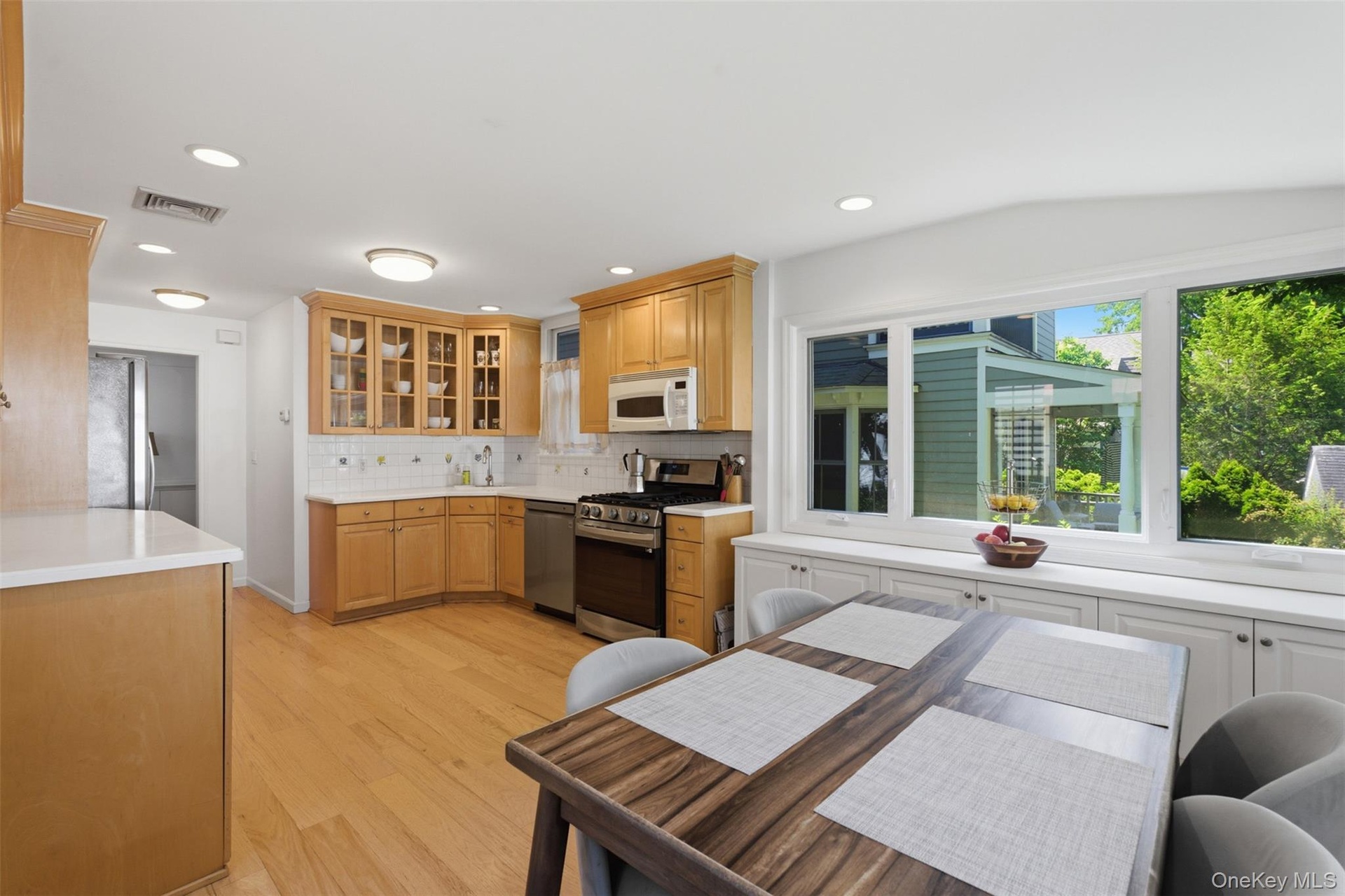 Hardwood flooring, light wood cabinetry, white countertops, built-in stainless steel appliances, and a wall of windows