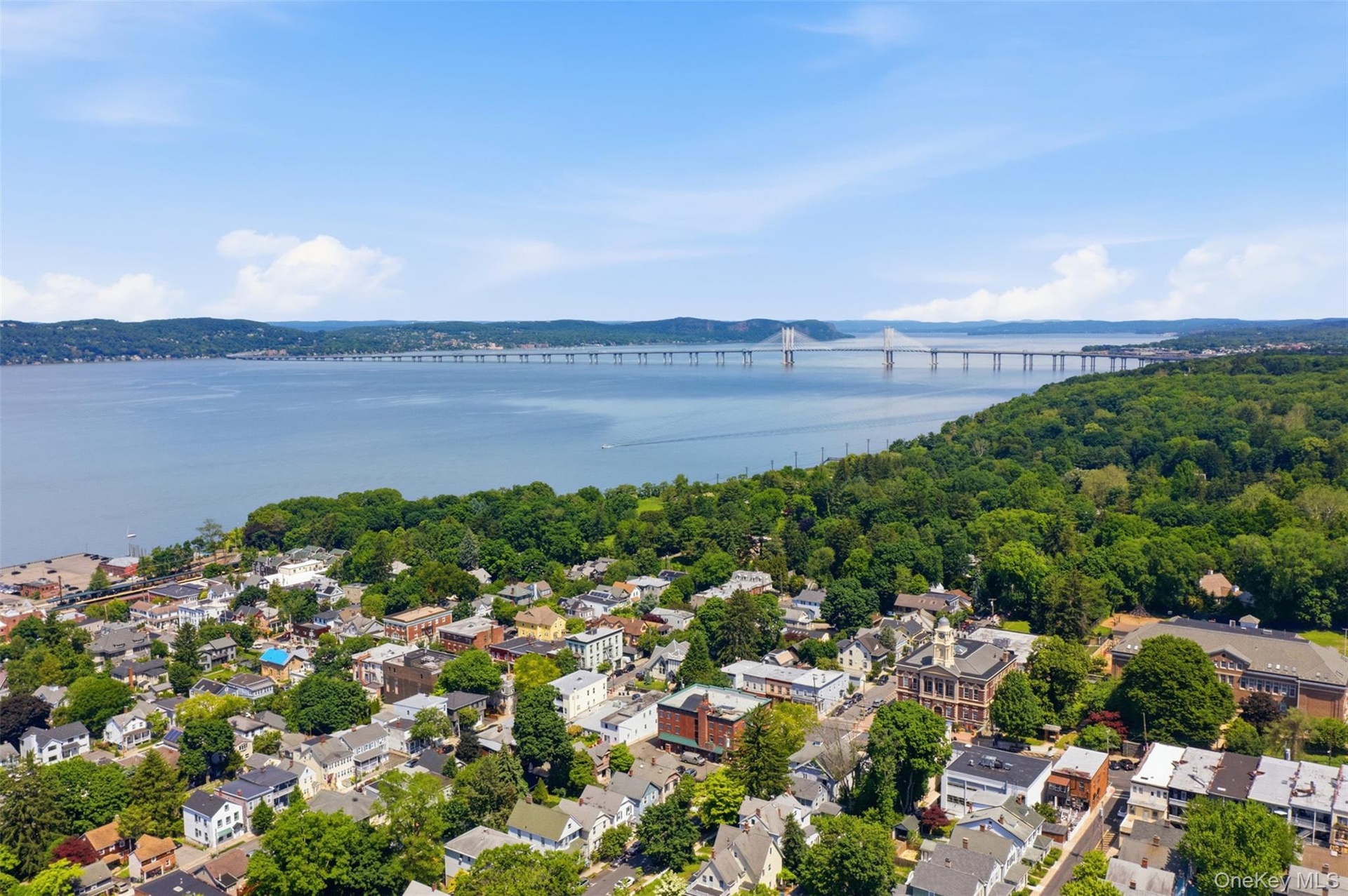 Waterfront setting with a long-span bridge, dense green tree canopy, and established residential structures