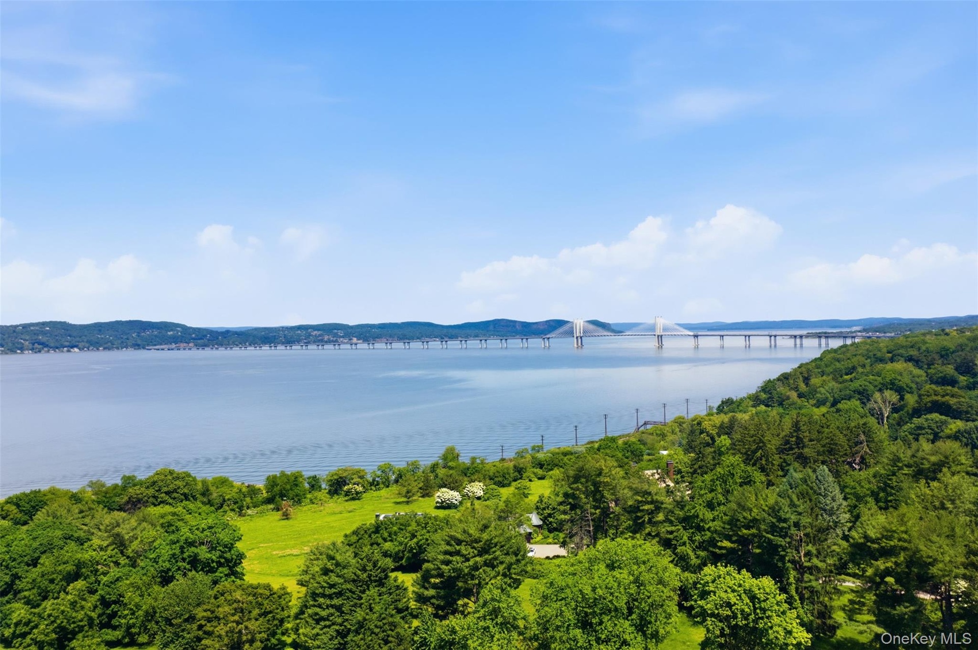 Expansive waterfront with distant bridge, lush green hills, and mature trees