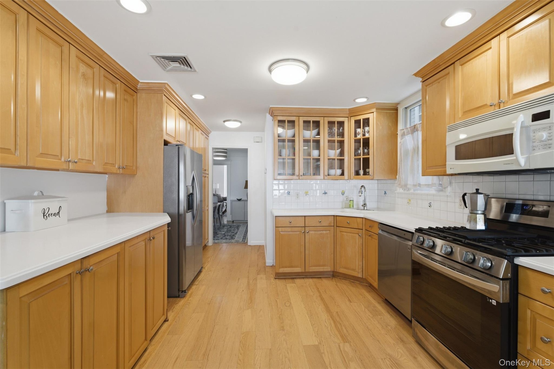 Hardwood flooring throughout, extensive wood cabinetry, white countertops, built-in stainless steel appliances, and recessed lighting
