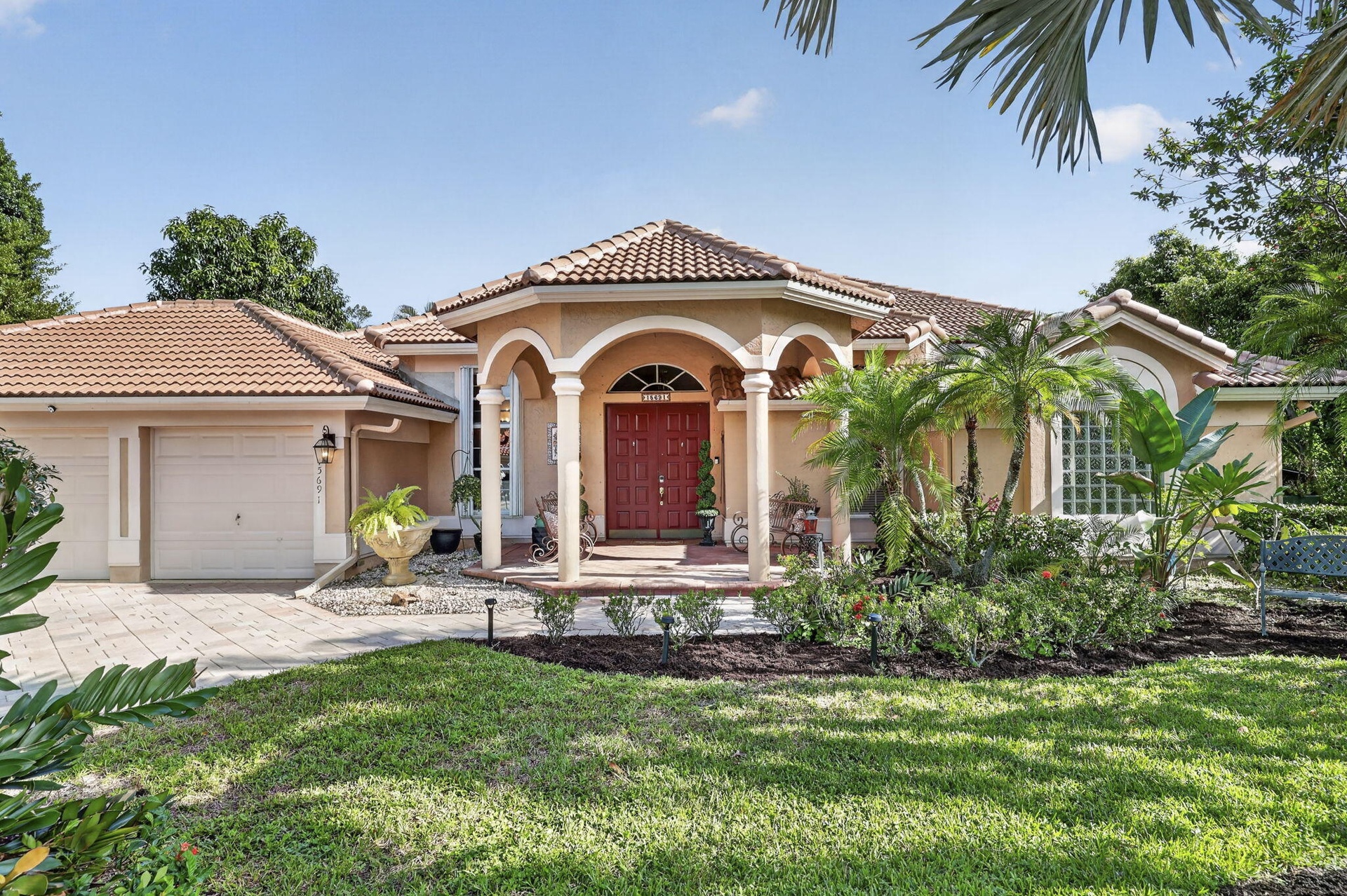 Mediterranean-style residence featuring a tile roof, arched entryway with columns, red double entry doors, a two-car garage, and mature landscaping