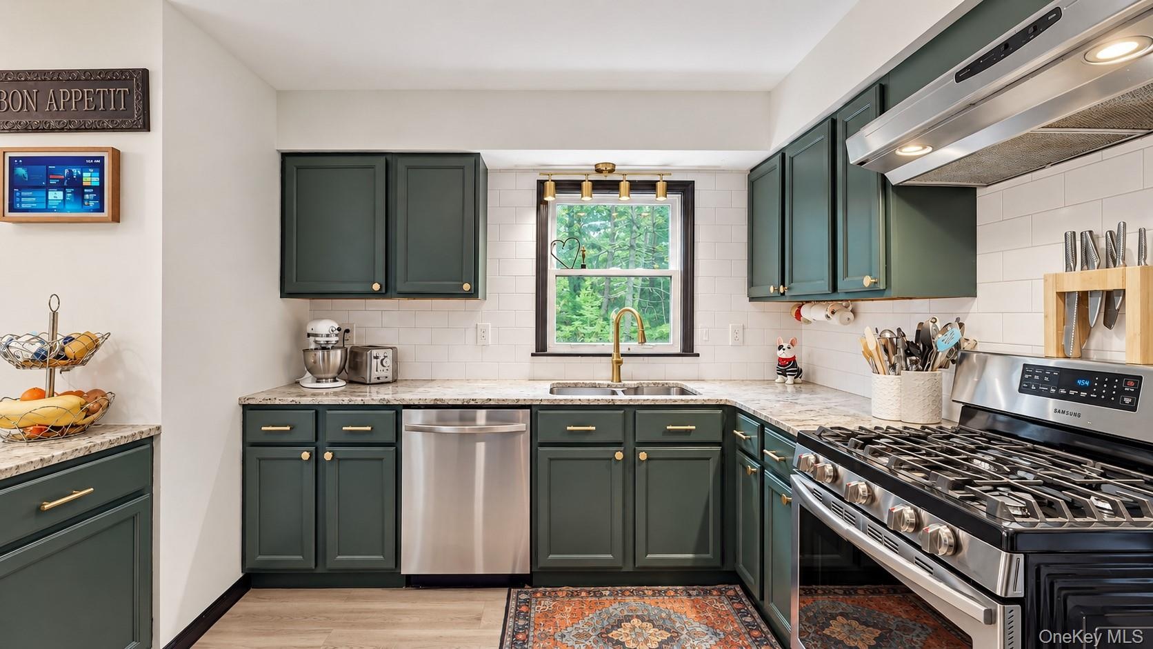 Kitchen with dark green cabinetry, white subway tile backsplash, light-colored countertops, and stainless steel appliances