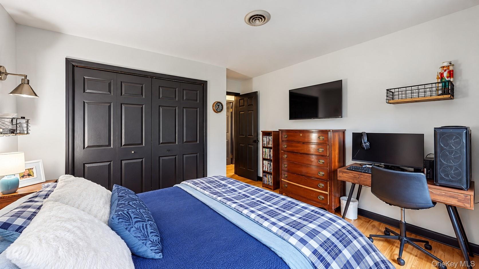Hardwood-style flooring, dark paneled bi-fold closet doors, wall-mounted light fixture, wall-mounted shelving unit, ceiling-mounted vent