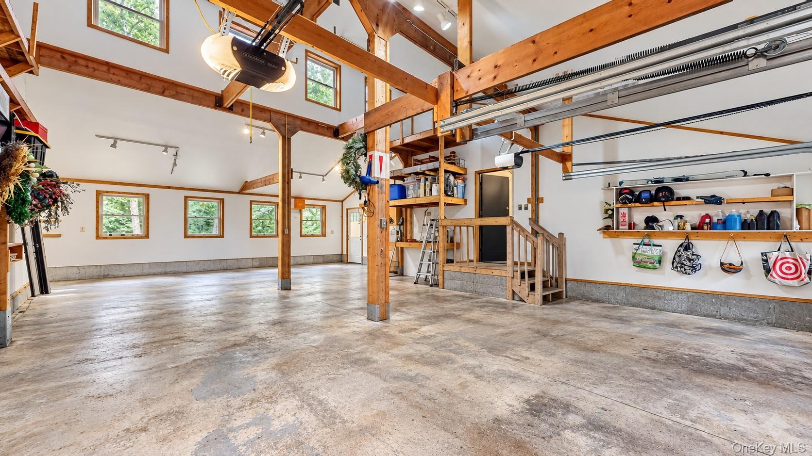 Spacious garage featuring exposed wood beams, multiple windows, a concrete floor, and built-in shelving