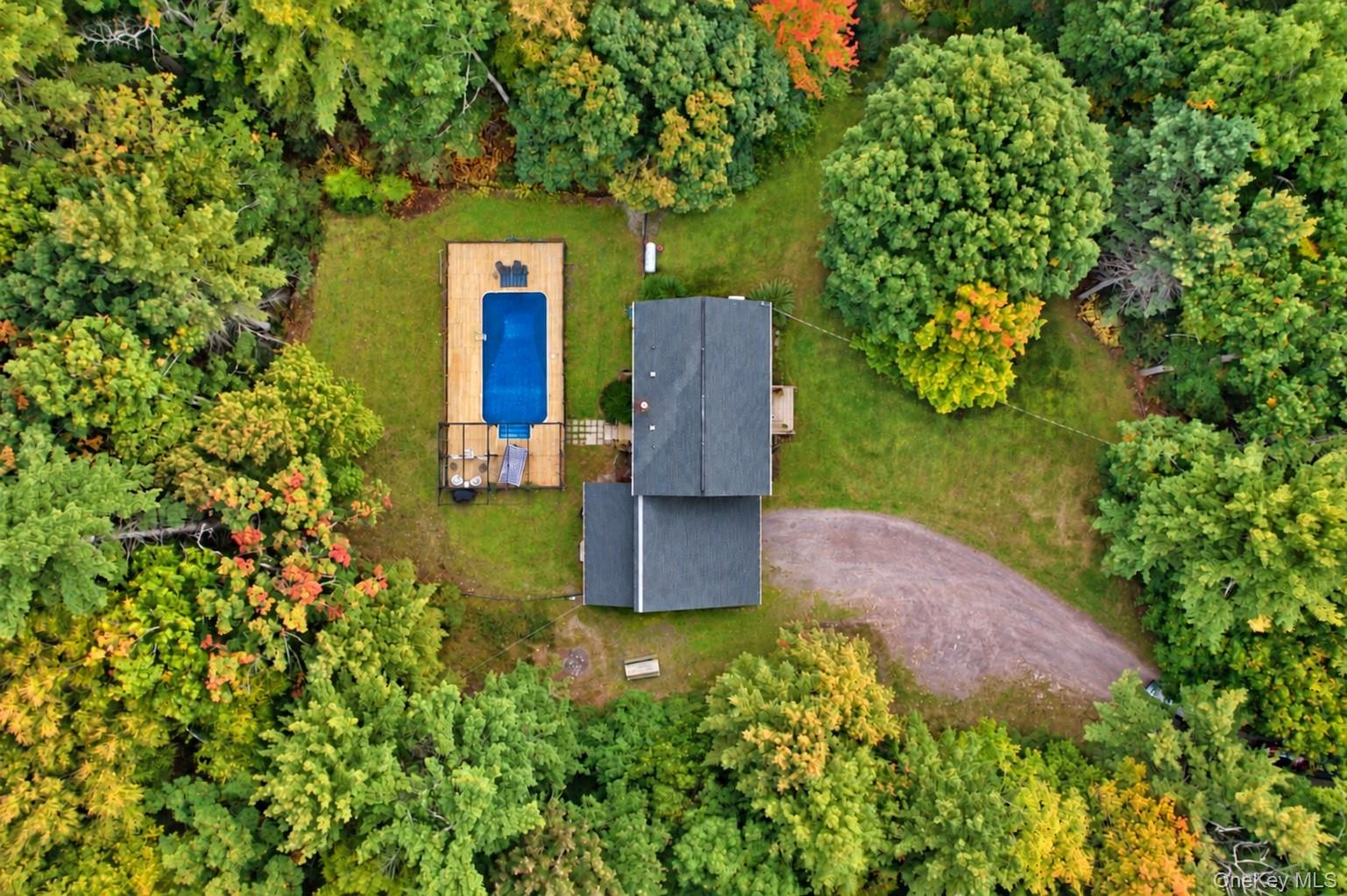 Expansive grounds with mature trees, a gravel driveway, a rectangular swimming pool, and a surrounding wood deck