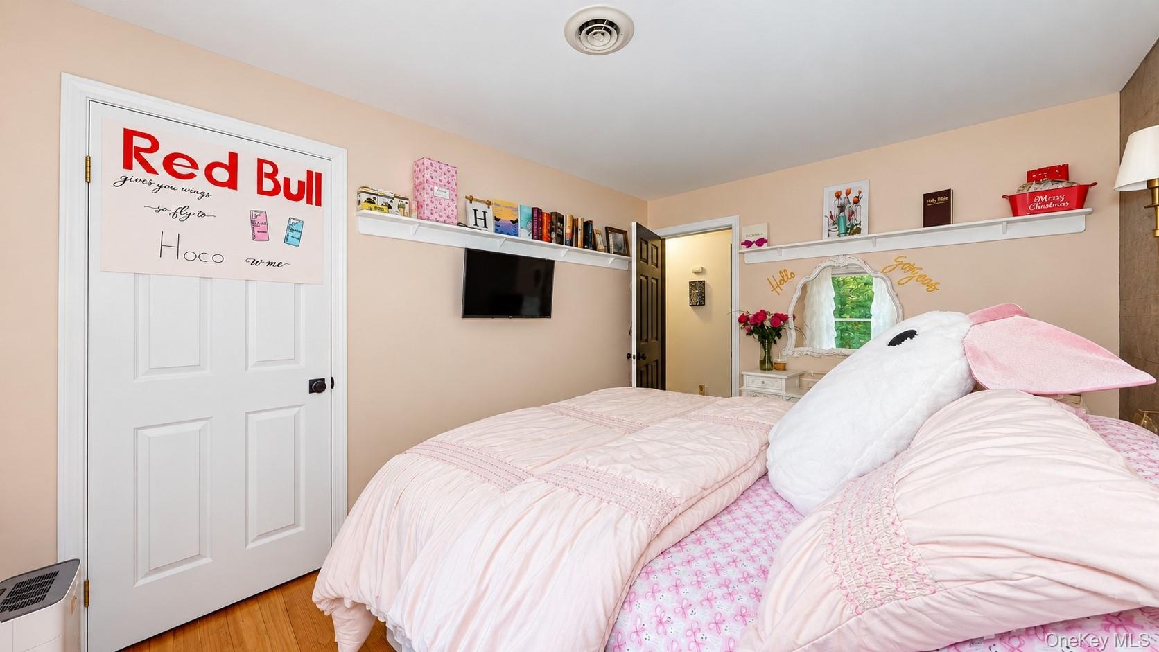 Light-toned wall paint, natural wood-finish flooring, white four-panel door with dark hardware, white wall-mounted shelving