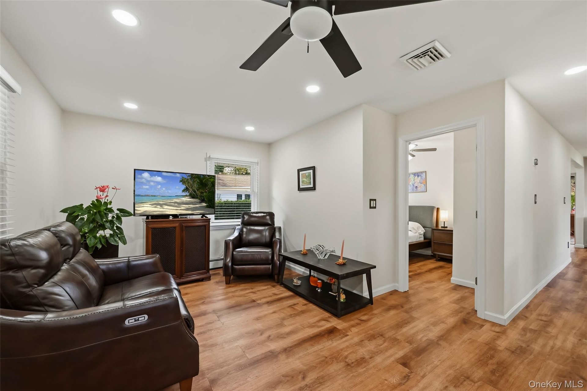 Spacious living room showcasing warm wood-finish flooring, recessed ceiling lighting, and a ceiling fan with integrated light fixture