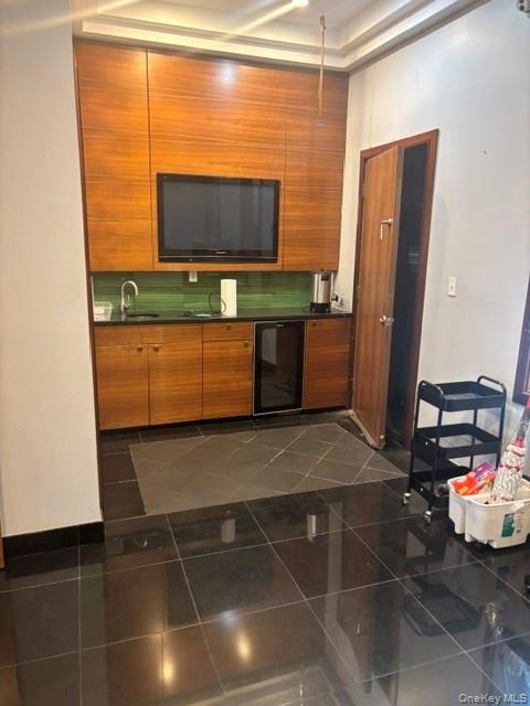 Wood-finish cabinetry with integrated television, black countertop, green tile backsplash, and a built-in beverage cooler