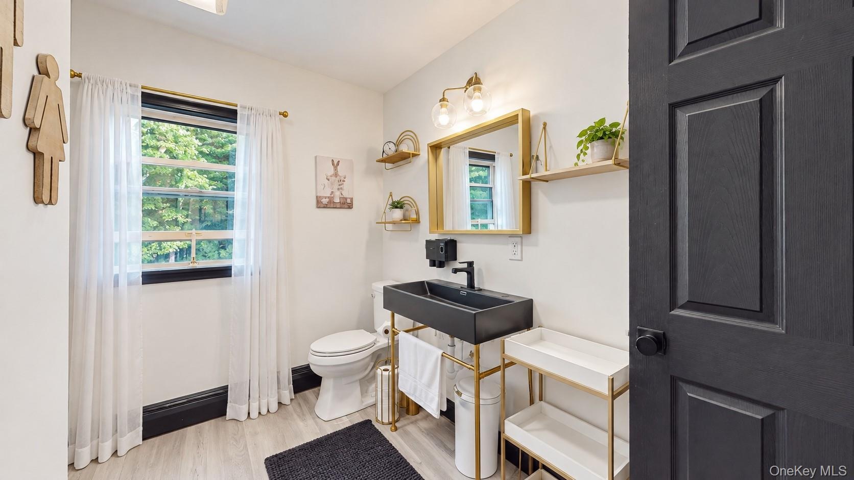 White interior walls with a black paneled door, light wood-finish flooring, and a modern black vanity with a vessel sink
