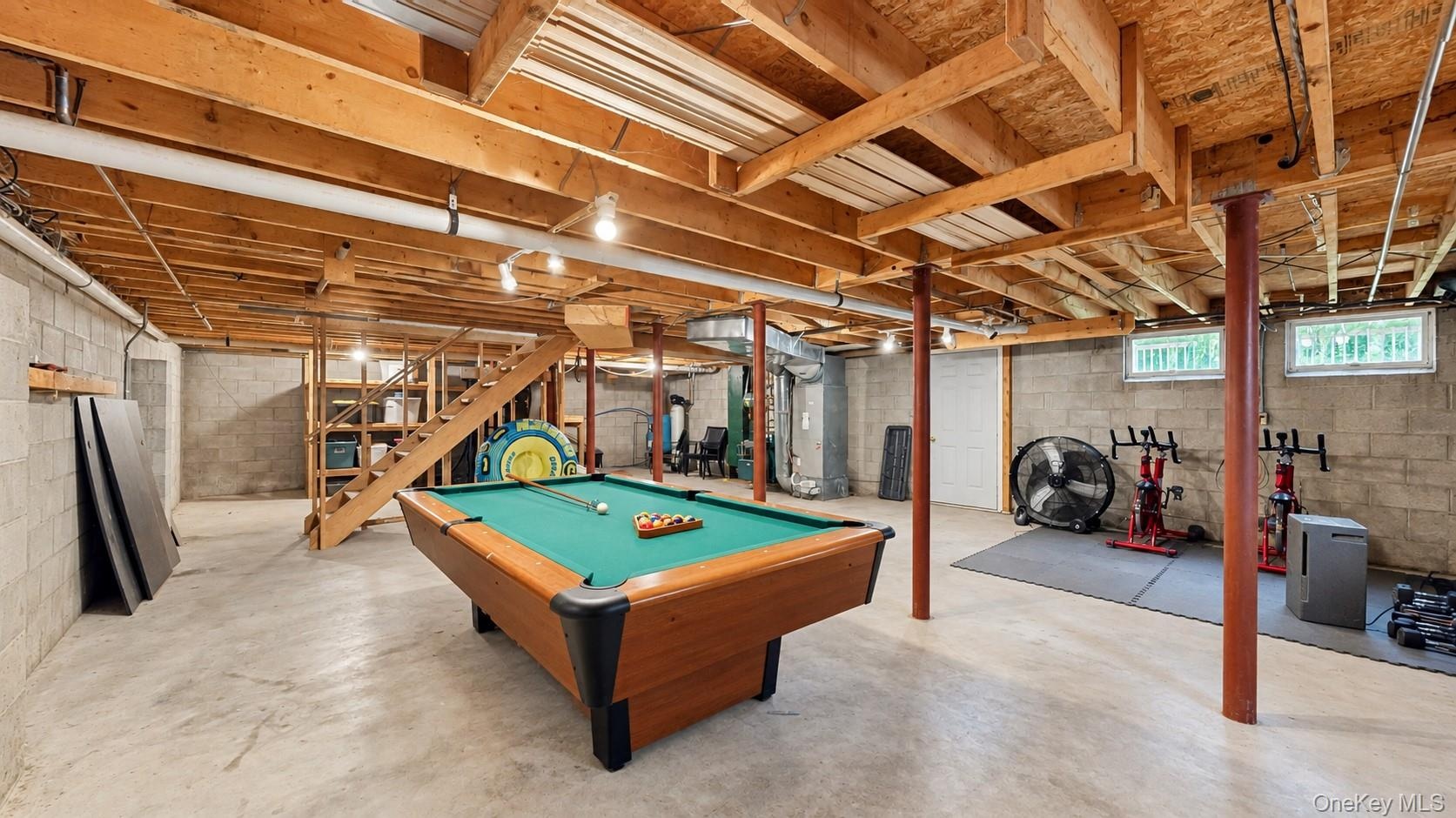 Concrete slab flooring, exposed wood beam ceiling, block wall construction, natural light windows, and open staircase