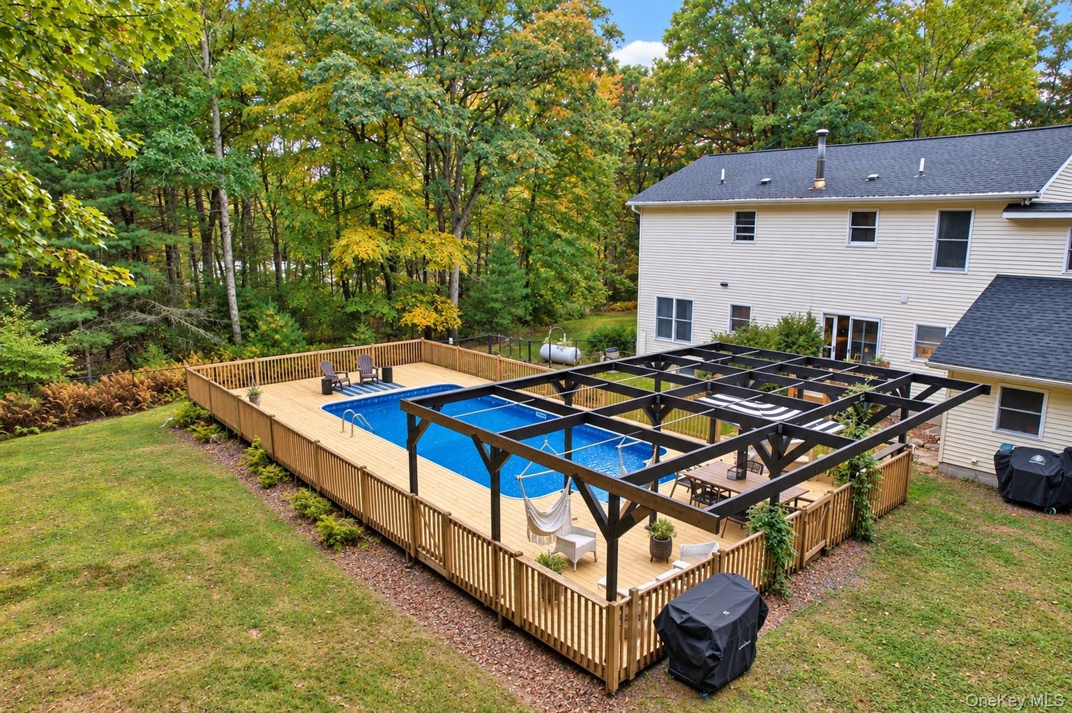 Expansive backyard featuring an in-ground pool, a surrounding wood deck, a wood privacy fence, and a dark-toned pergola