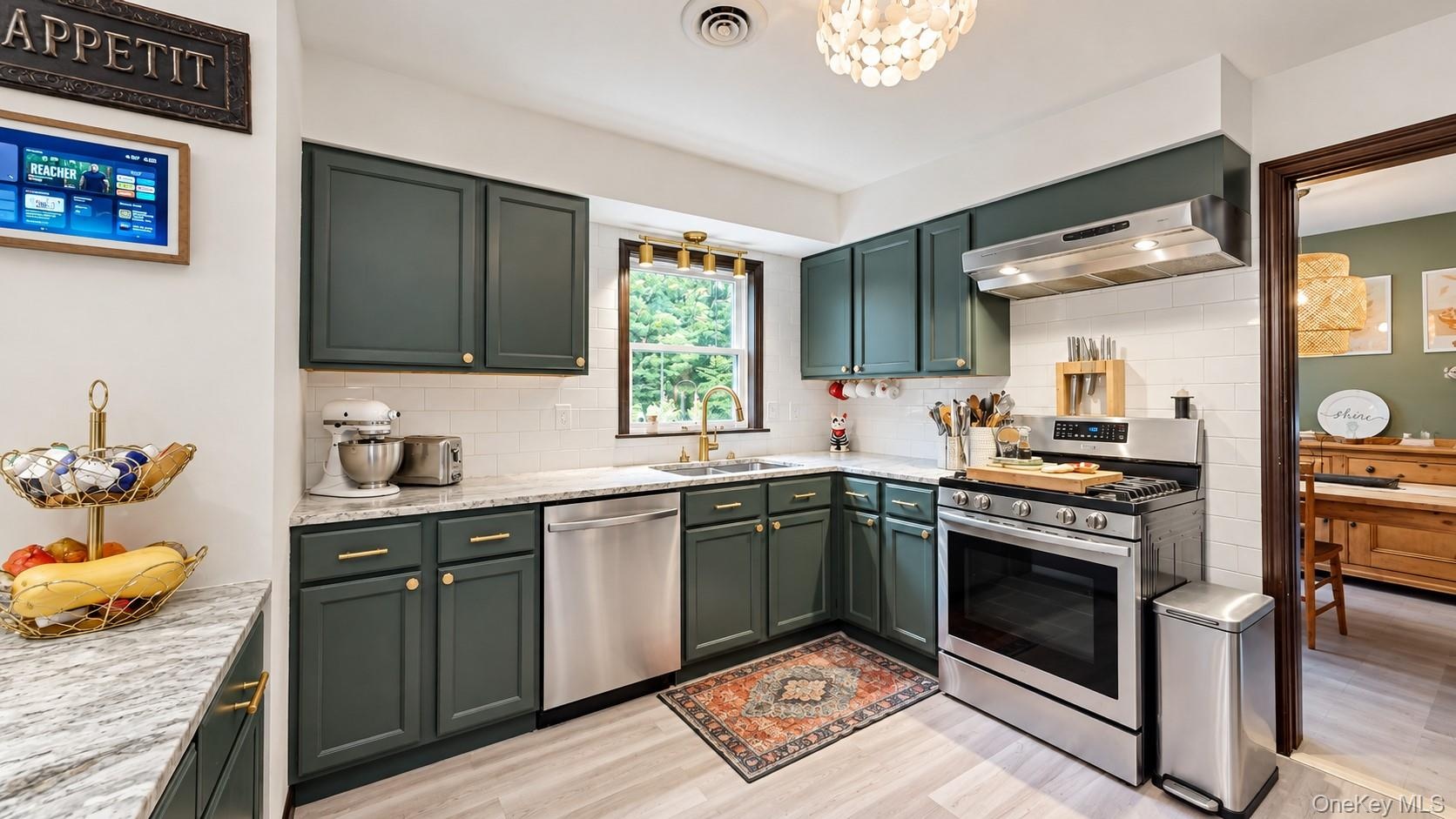 Kitchen featuring dark green cabinetry, light-toned countertops, white subway tile backsplash, stainless steel appliances, and wood-finish flooring