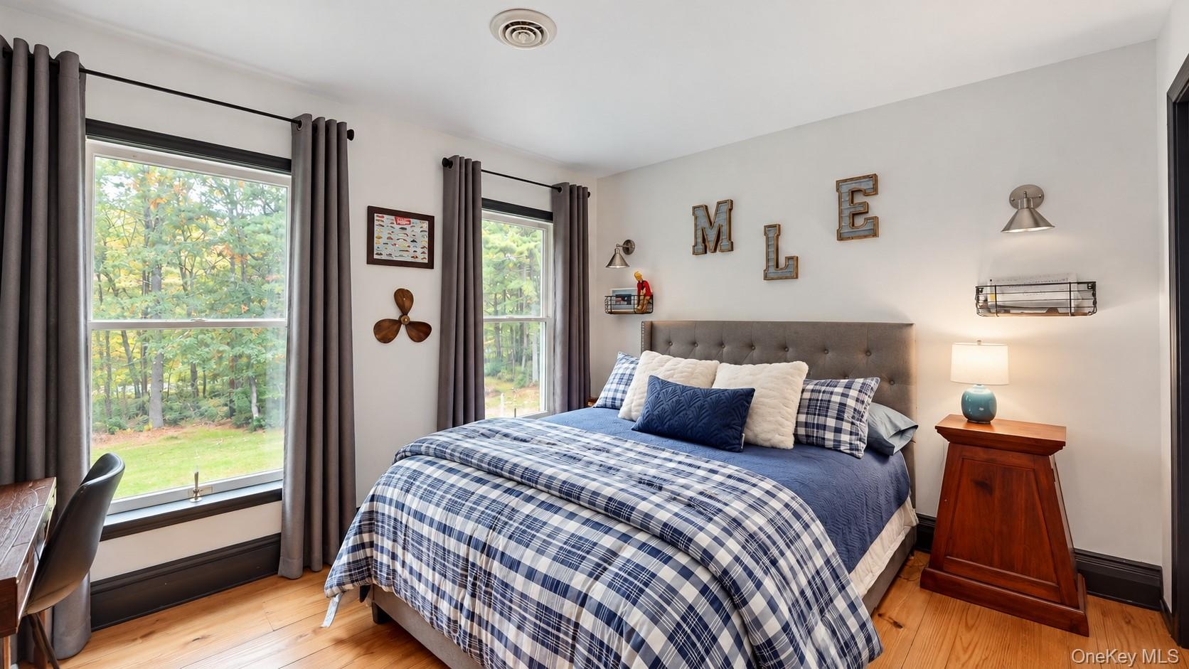 Hardwood flooring, two large windows, a tufted upholstered headboard, and recessed ceiling lighting