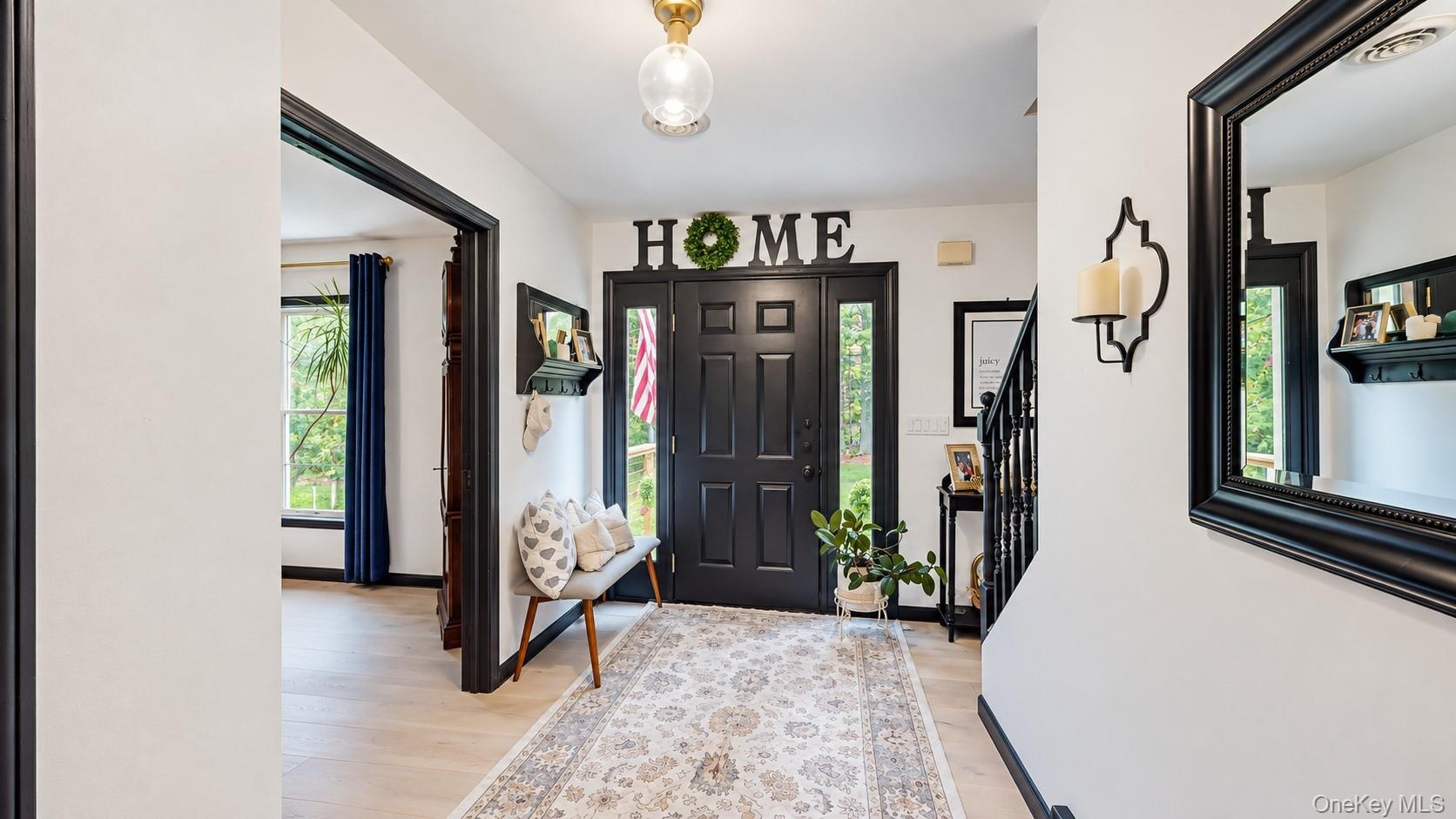 Entryway featuring a black paneled door with sidelights, wood-finish flooring, and a staircase with dark banisters