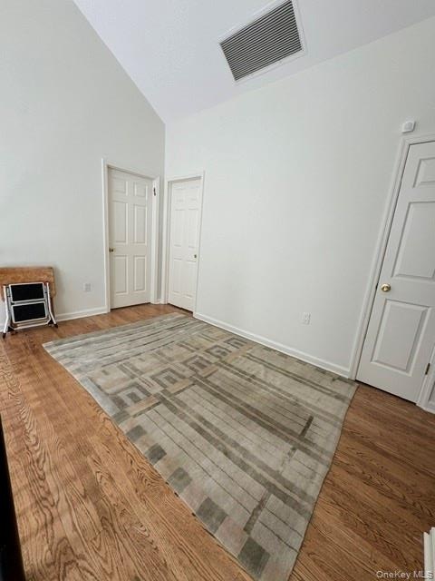 Vaulted ceiling with a ceiling vent, wood-finish flooring, and white paneled doors