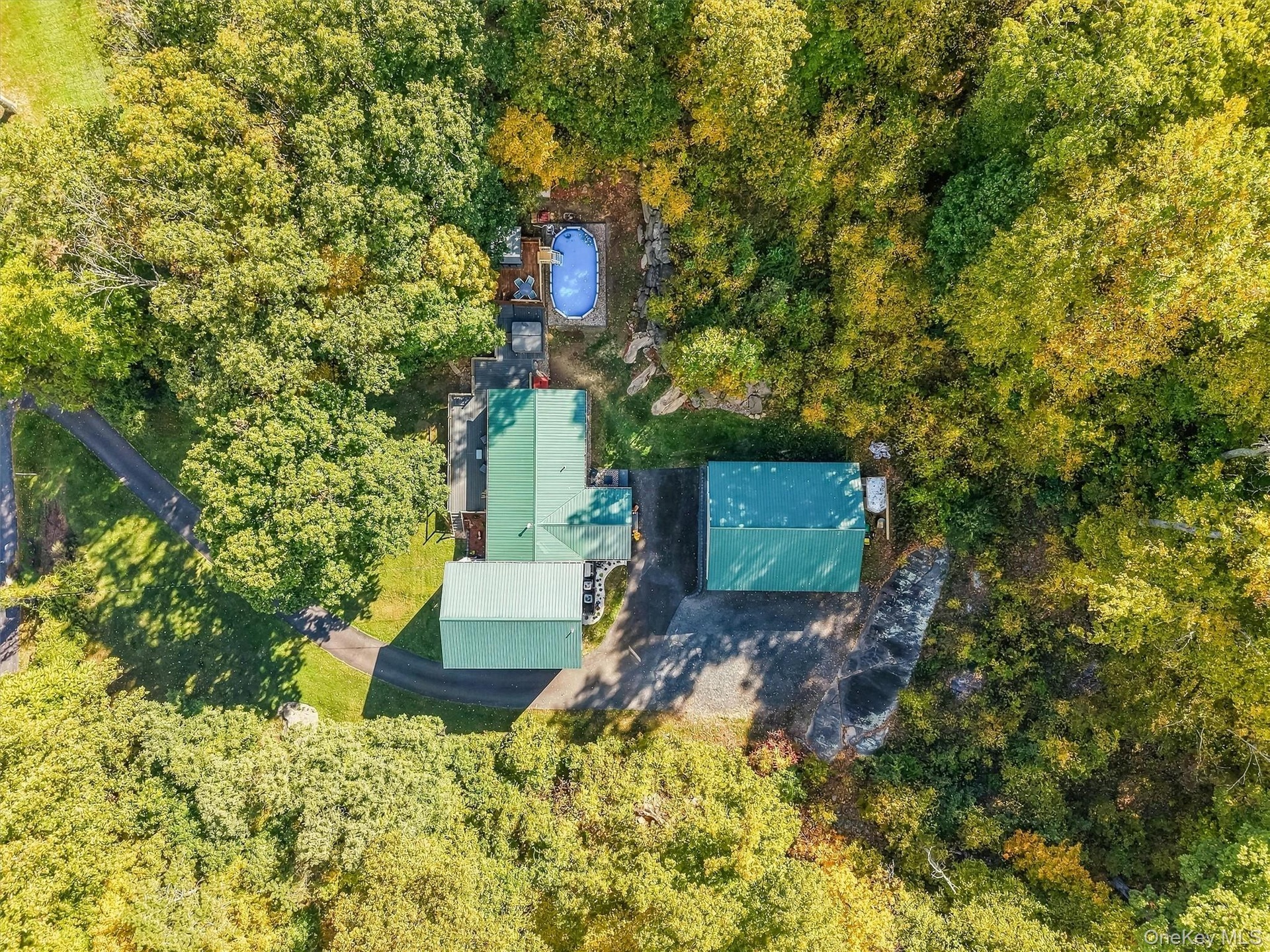 Lush natural surroundings with mature trees, multiple outbuildings, an above-ground pool with surrounding decking, and a paved driveway
