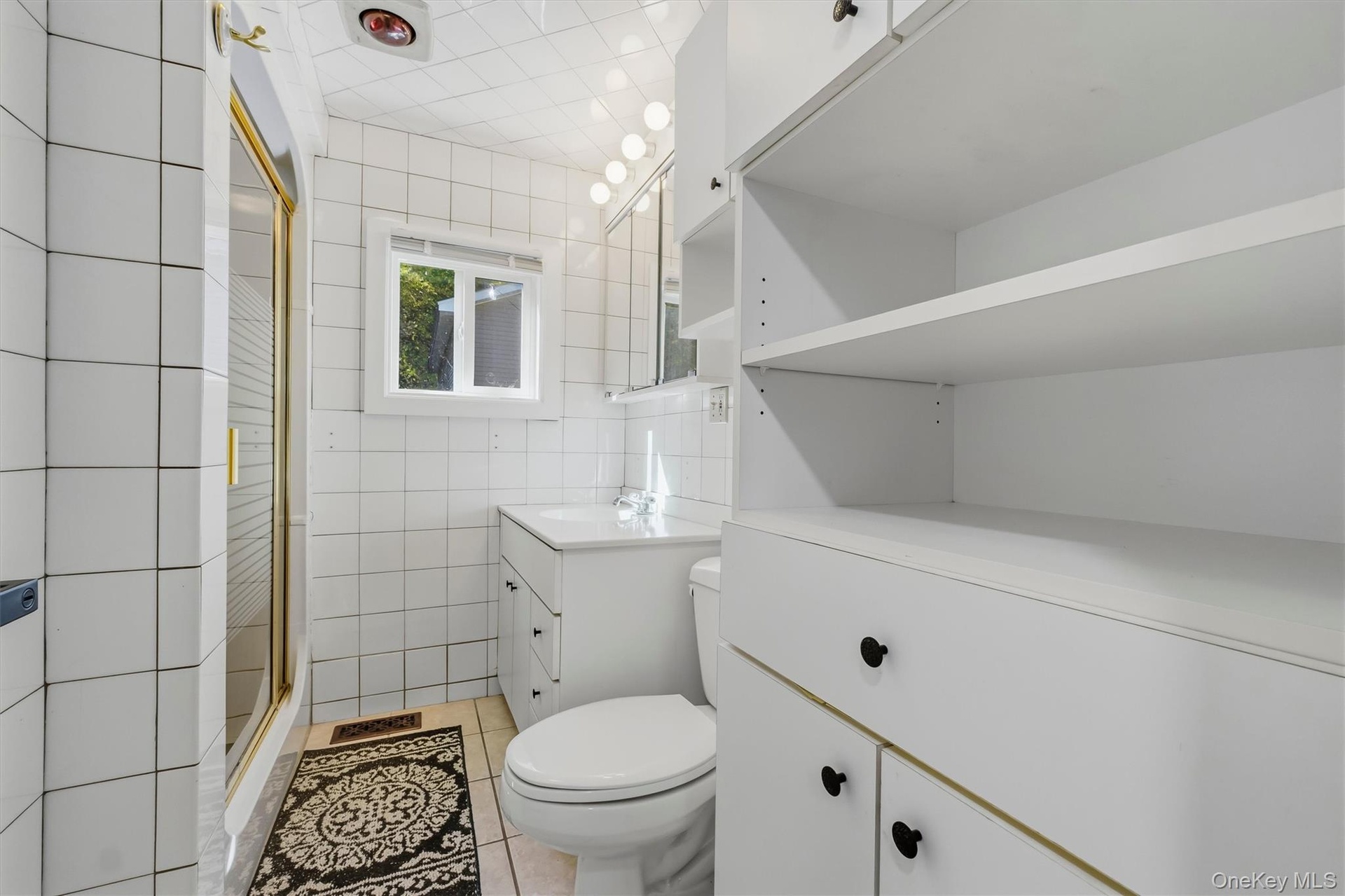 White tiled bathroom featuring a shower with a gold-toned frame, a vanity with an integrated sink, a built-in toilet, and extensive white cabinetry